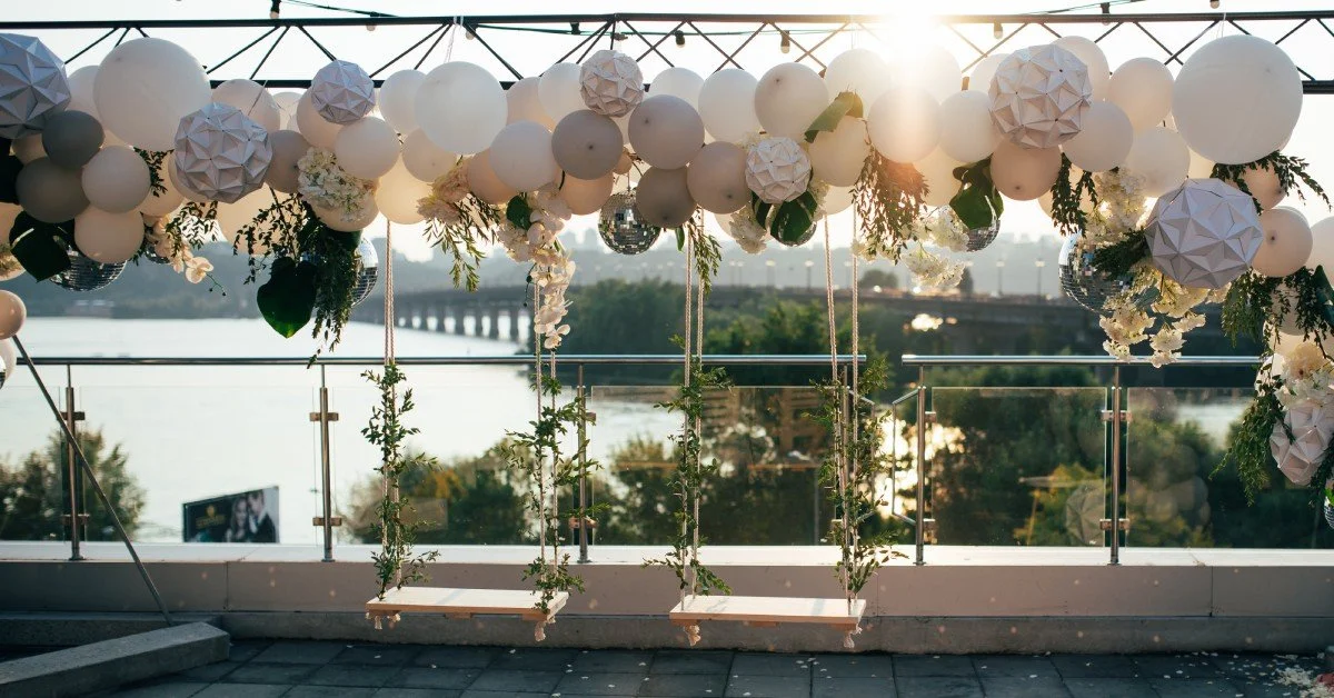 An outdoor party set up with many different balloons hanging from scaffolding. Two swings also hang from the scaffolding.