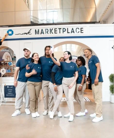 A group of people, all in the same shirt, taking a selfie in front of an archway that says "Marketplace" above them.