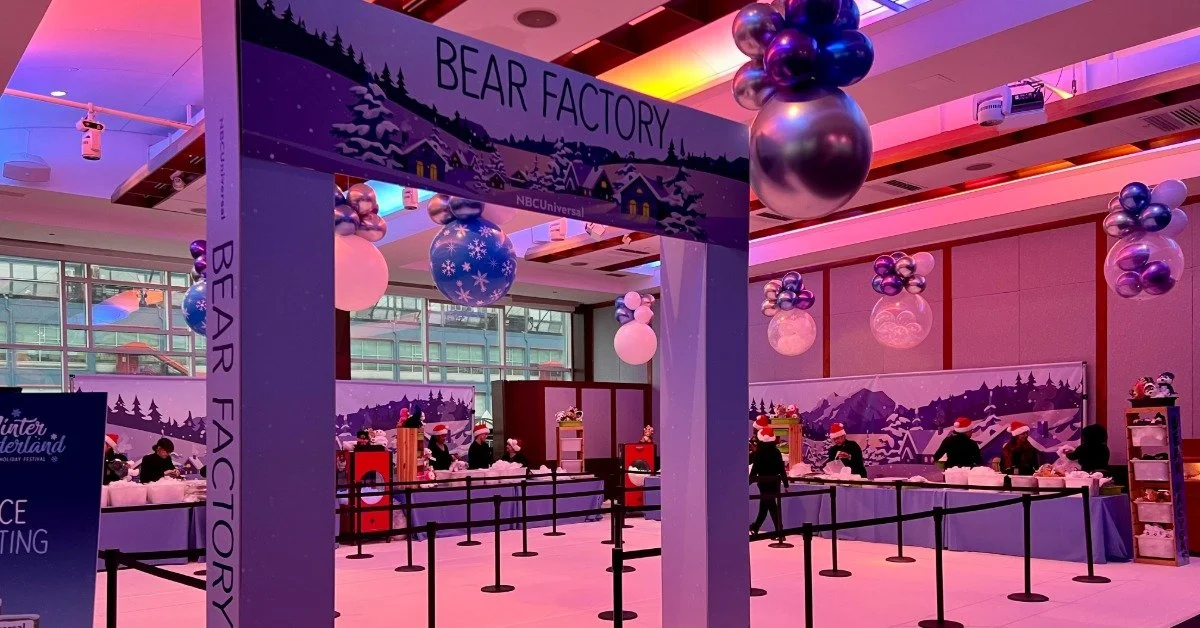 A queue cordoned off by extendible barriers. The queue has an archway at its beginning that says "Bear Factory."