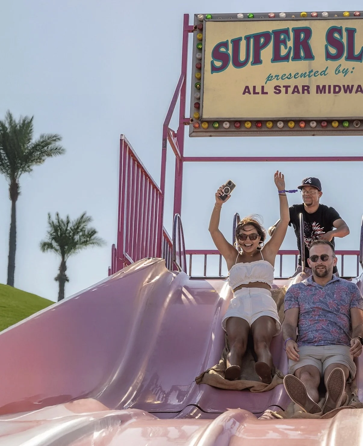 A man and a woman going down a super slide at a carnival. There is a slide employee standing just behind them.
