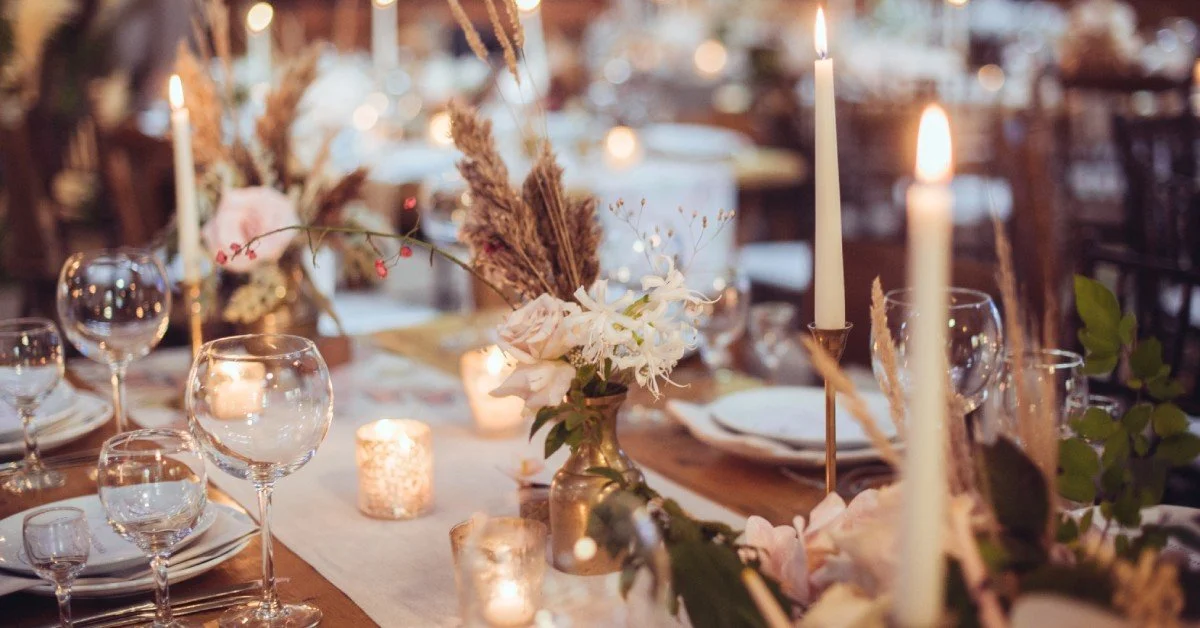 An elegant table setting with multiple lit candles. There are multiple glasses, plates, and silverware at each seat.