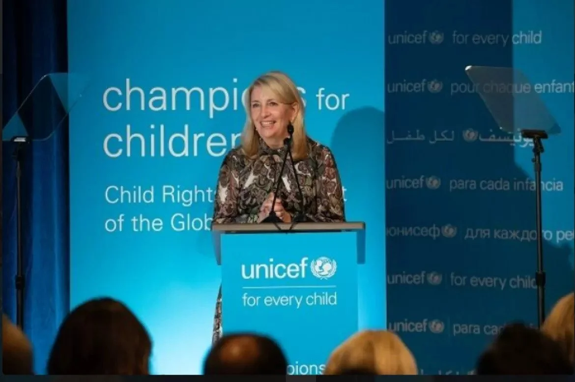A well-dressed woman standing behind a podium with a microphone attached to it giving a speech for UNICEF.