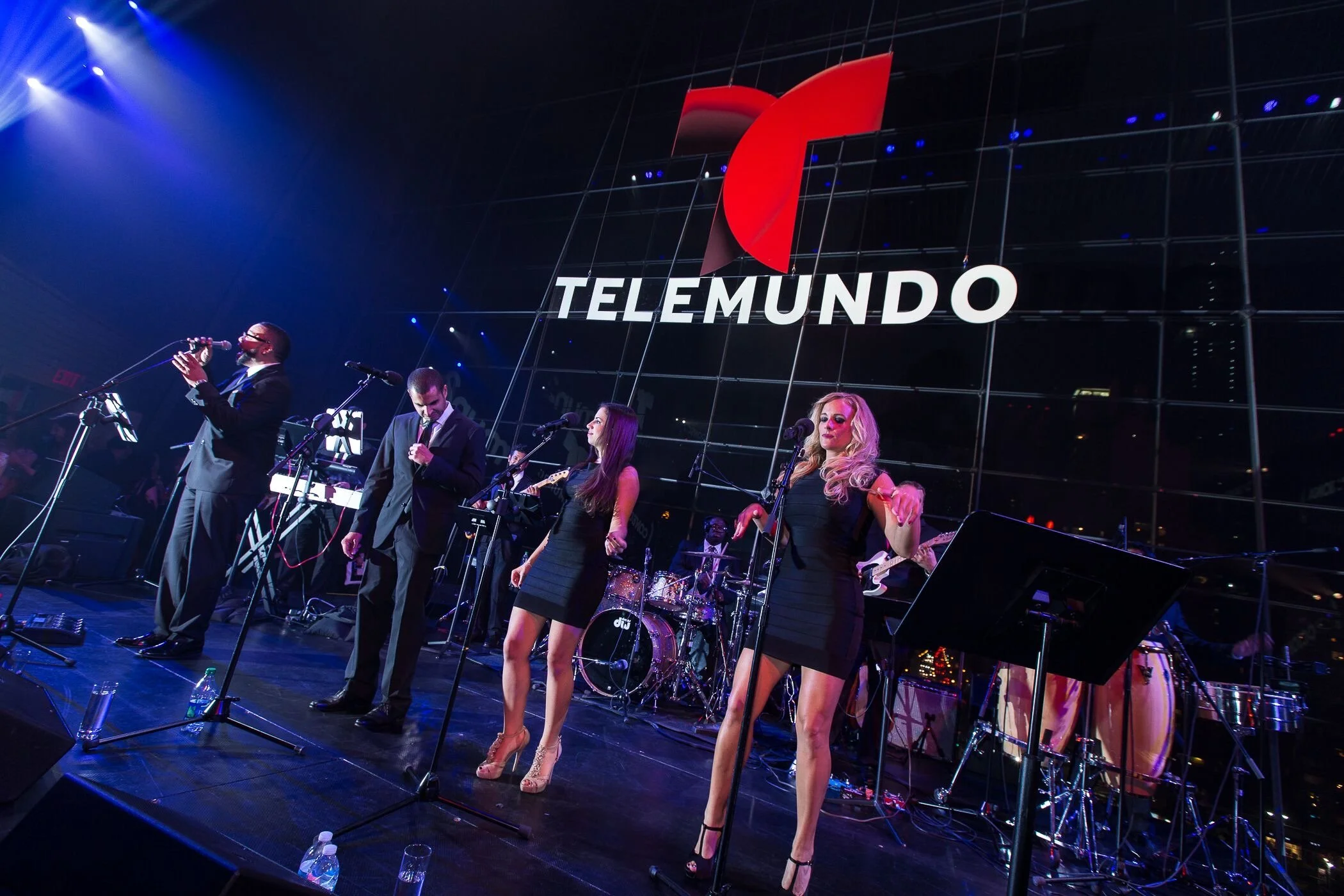 A band on stage with four different singers. There is a large sign right behind them that says "Telemundo."