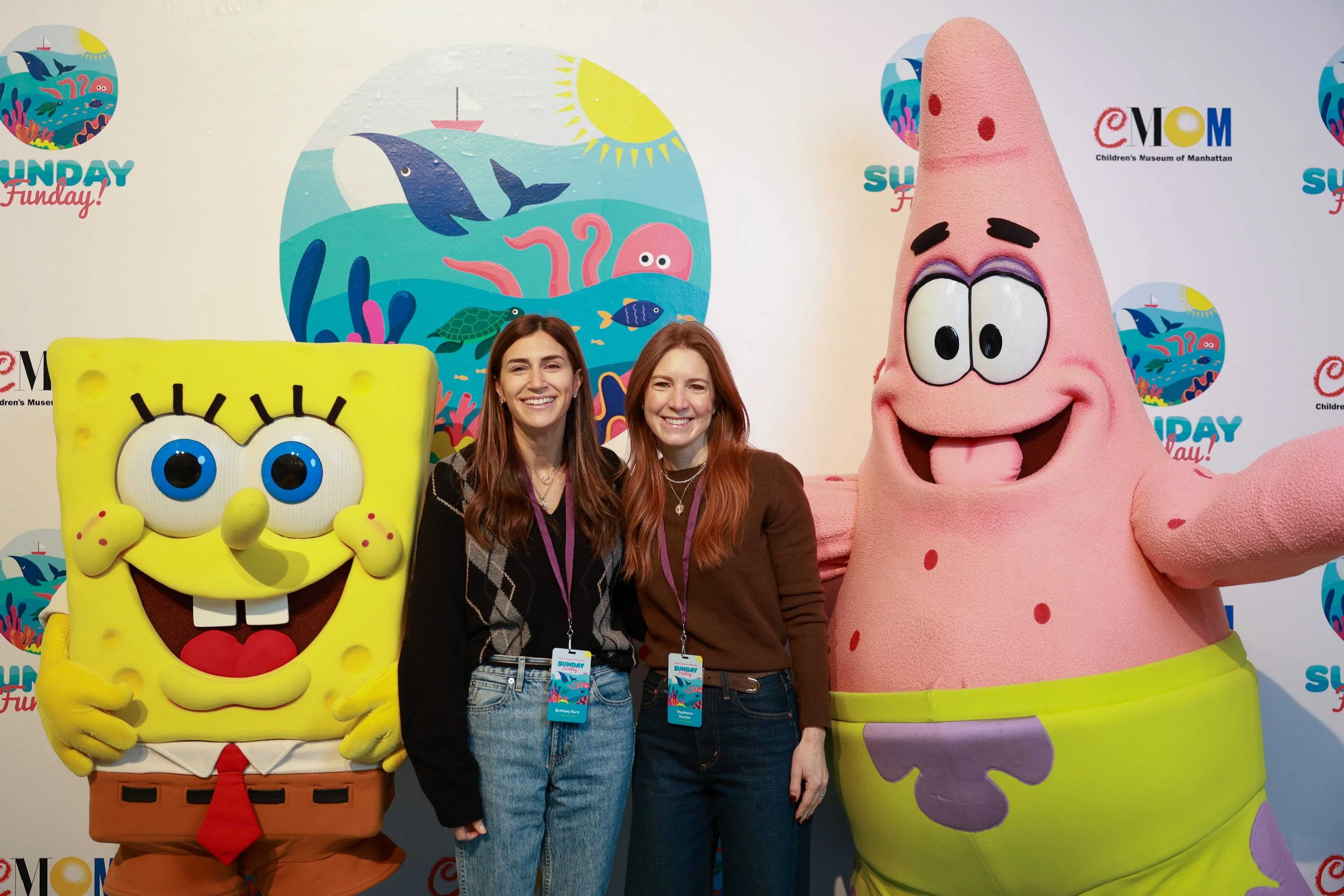 Two women posing for a photo as they stand in between people in mascot costumes of Spongebob and Patrick.