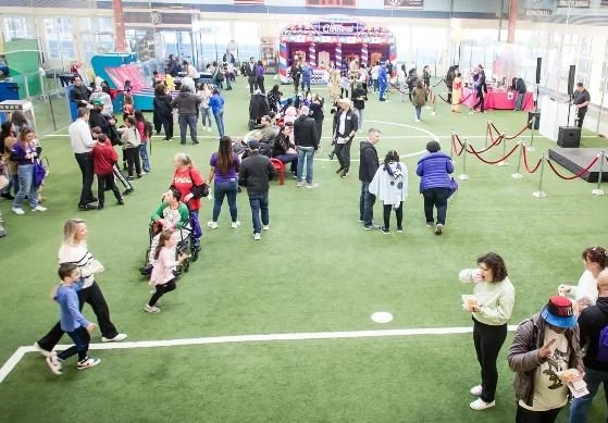 A large group of people walking around an indoor soccer field that has been repurposed for a convention.