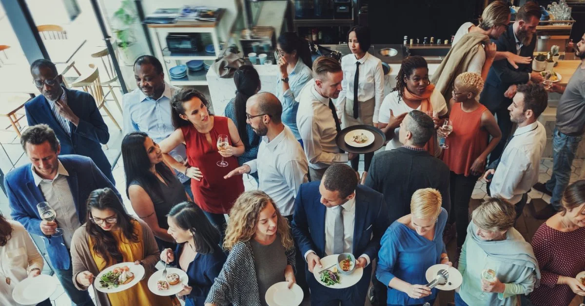 A large social event in a restaurant with many people dressed well and standing close to one another.
