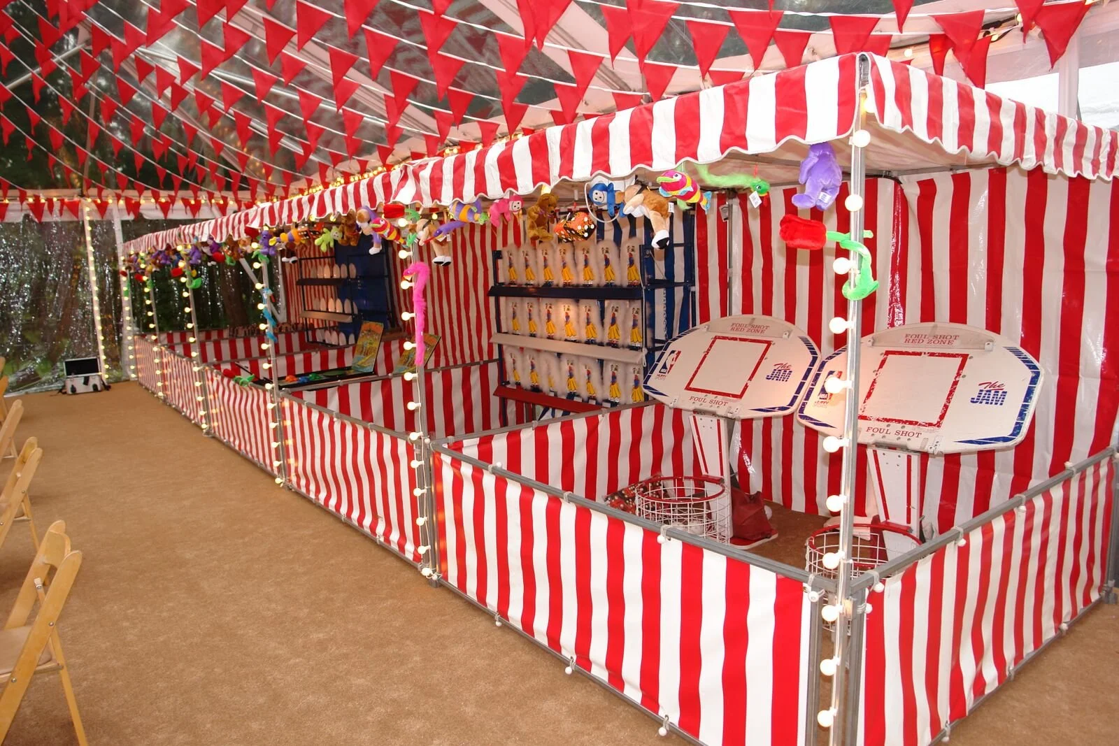 A row of red and white striped carnival tents. Inside the tents are various carnival games set up for event-goers.