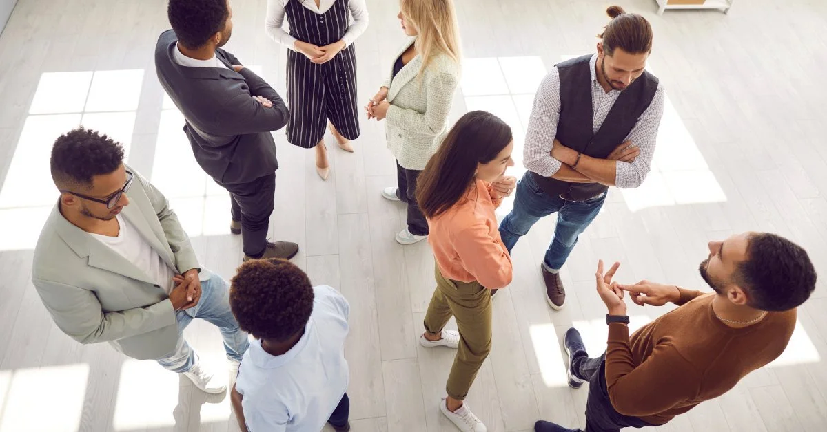 Three separate groups of well-dressed people standing in an empty, white room talking in between each other.