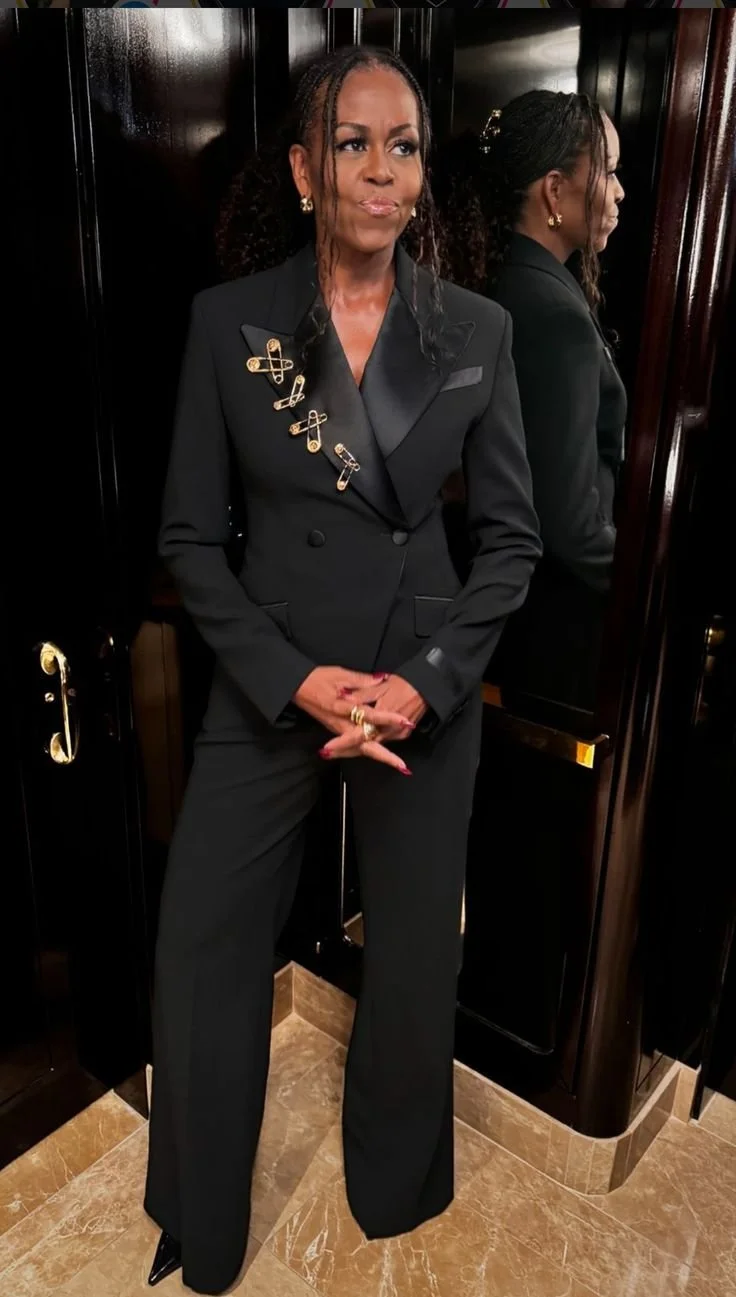 Woman wearing a black  blazer styled with a cluster of gold safety pin brooches arranged along the lapel