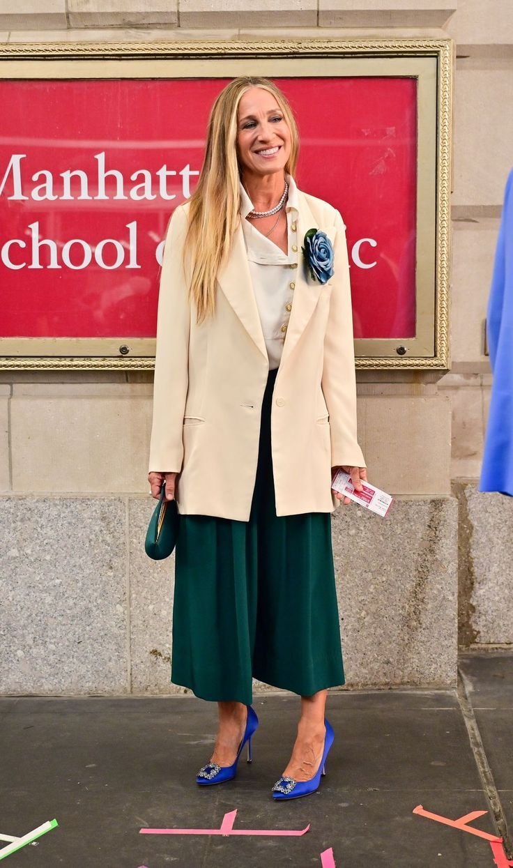 Woman wearing a cream-colored oversized blazer with a green forest maxi skirt and a statement blue brooch pinned to the blazer, accessorised with a dark green handbag and blue heels