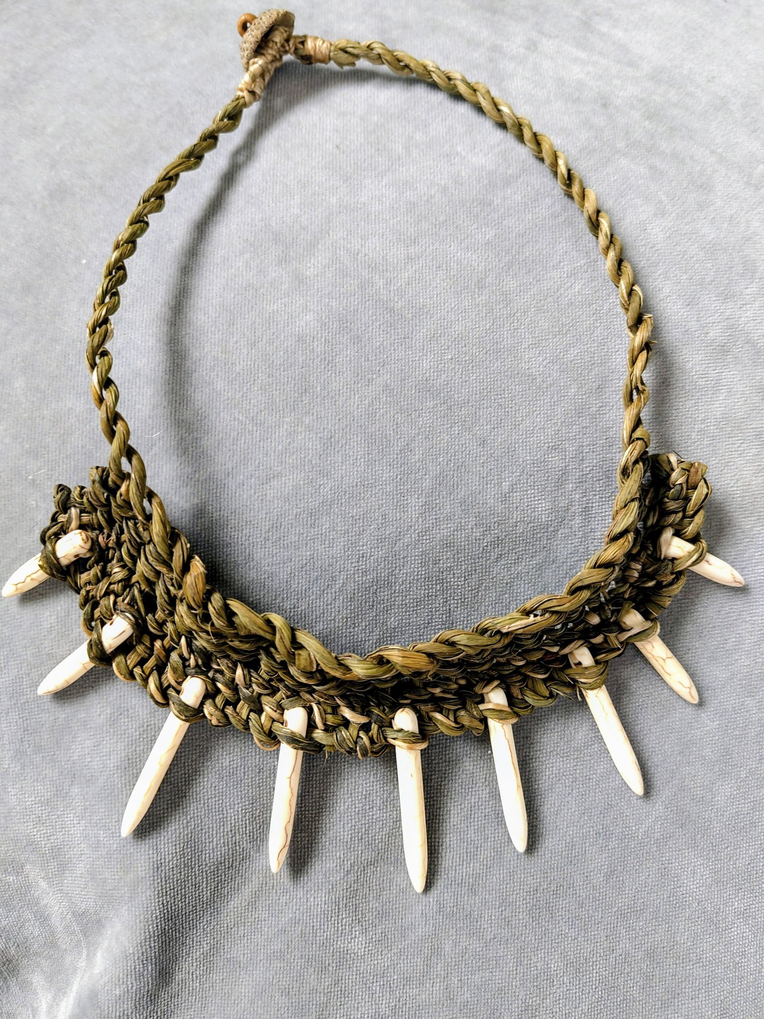 Handflätat halsband av mörkgrön säv med hängande spetsar av vitt horn