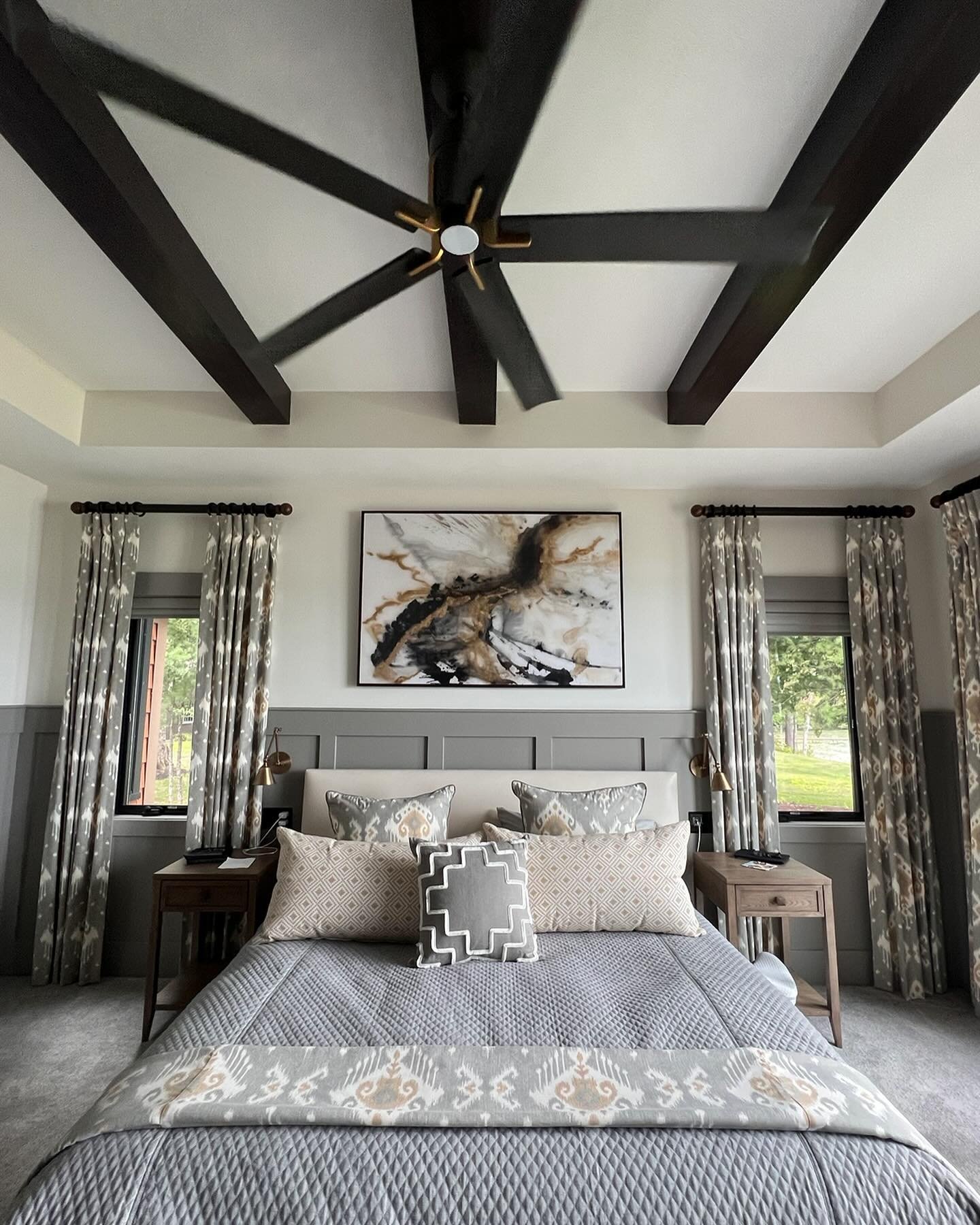 Cozy elegance meets functionality in this bedroom design. Custom bedding and coordinating blackout draperies create a serene atmosphere, while the artwork is perfectly sized to fit above the bed. Faux beams add a touch of architectural charm, tying t