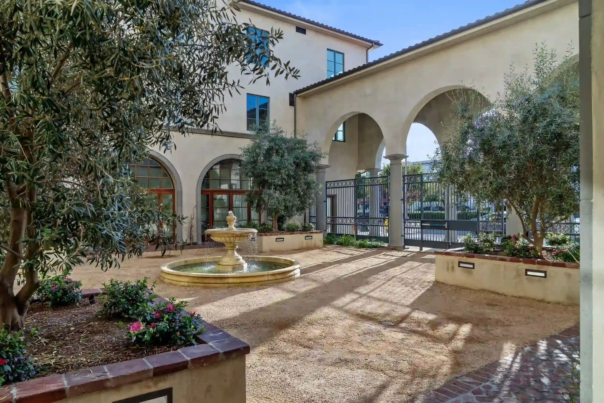 Landscaped courtyard at Brantwood senior apartments in Pasadena’s Playhouse Village, featuring a fountain, arched entryways, olive trees, and Spanish-style architecture.