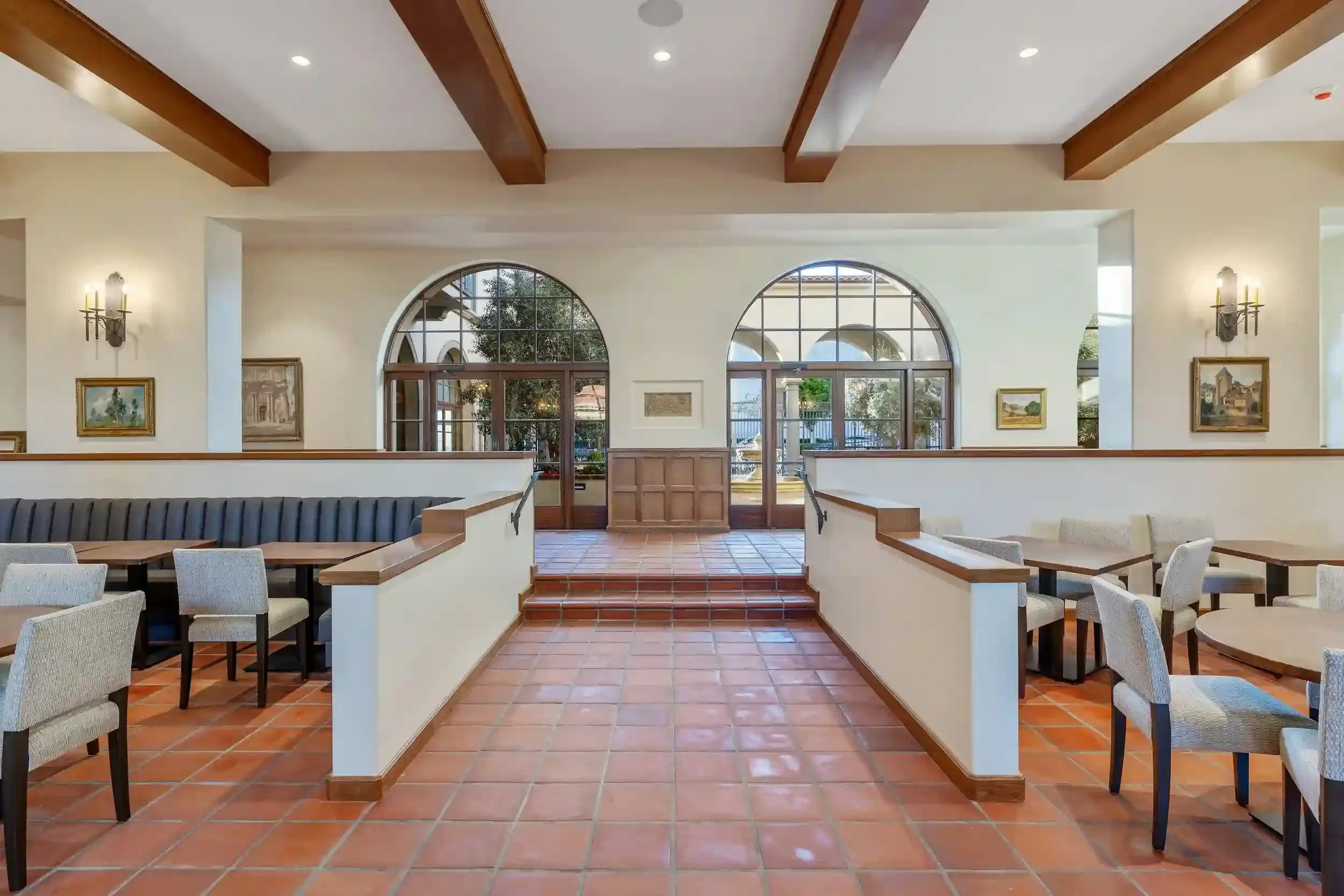 Dining and community room at Brantwood senior apartments in Pasadena’s Playhouse Village, featuring terracotta tile floors, arched windows, wood beams, and shared seating areas.