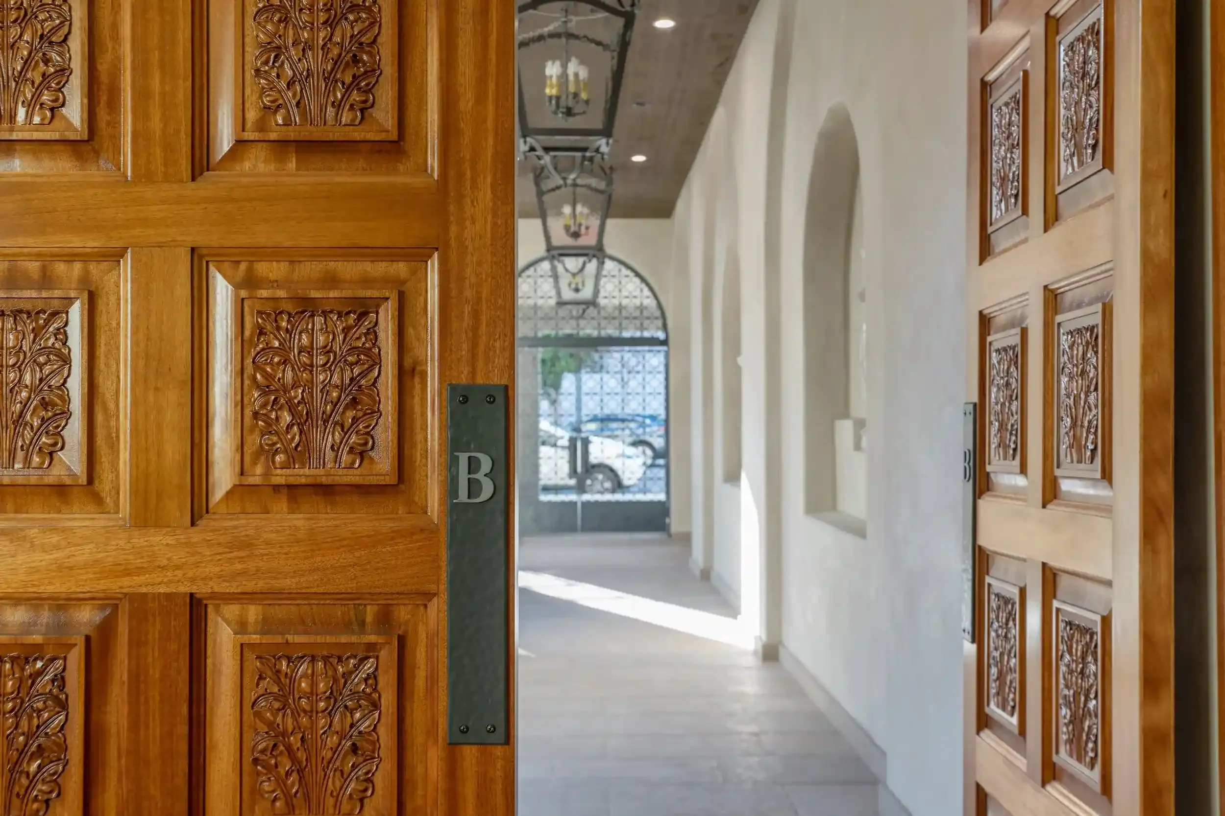 Ornate wood entry doors at Brantwood senior apartments in Pasadena’s Playhouse Village, opening into a bright arched corridor with Spanish-style architectural details.