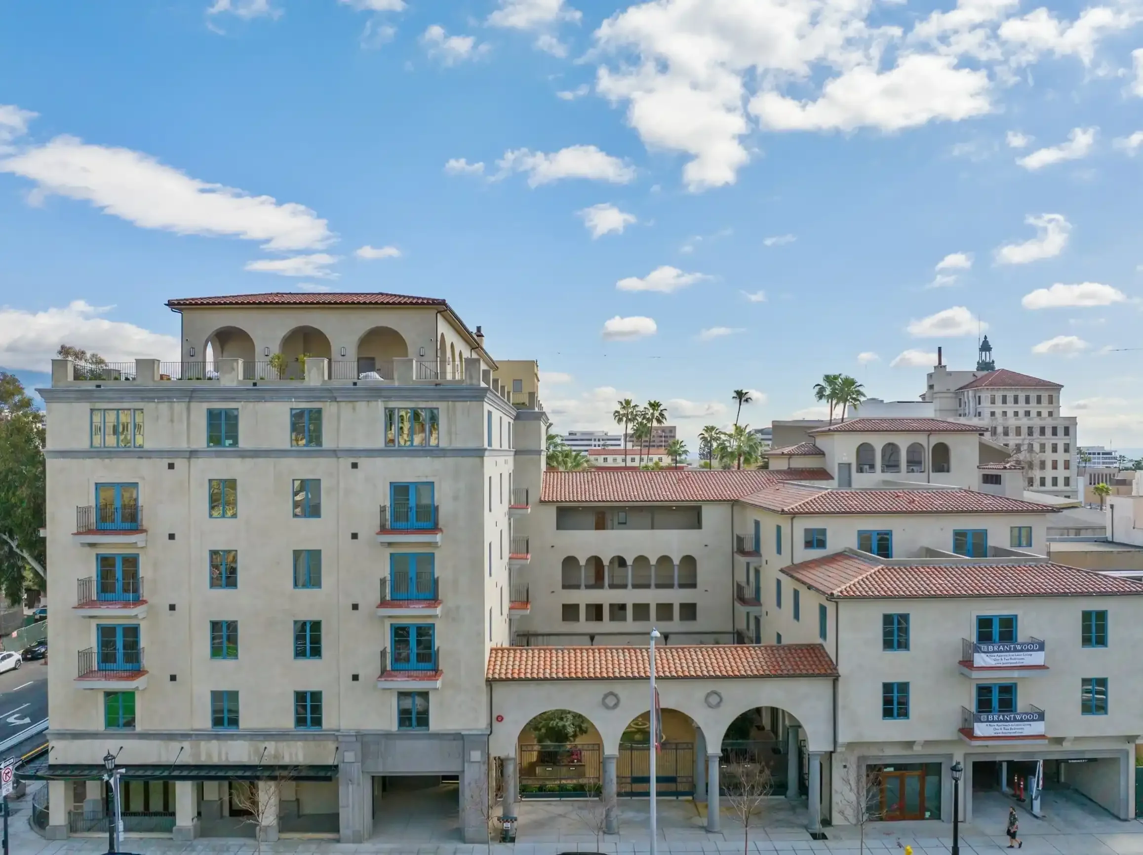 Exterior view of Brantwood senior apartments in Pasadena’s Playhouse Village, featuring Spanish-style architecture, arched entryways, blue-trimmed windows, and rooftop terraces.