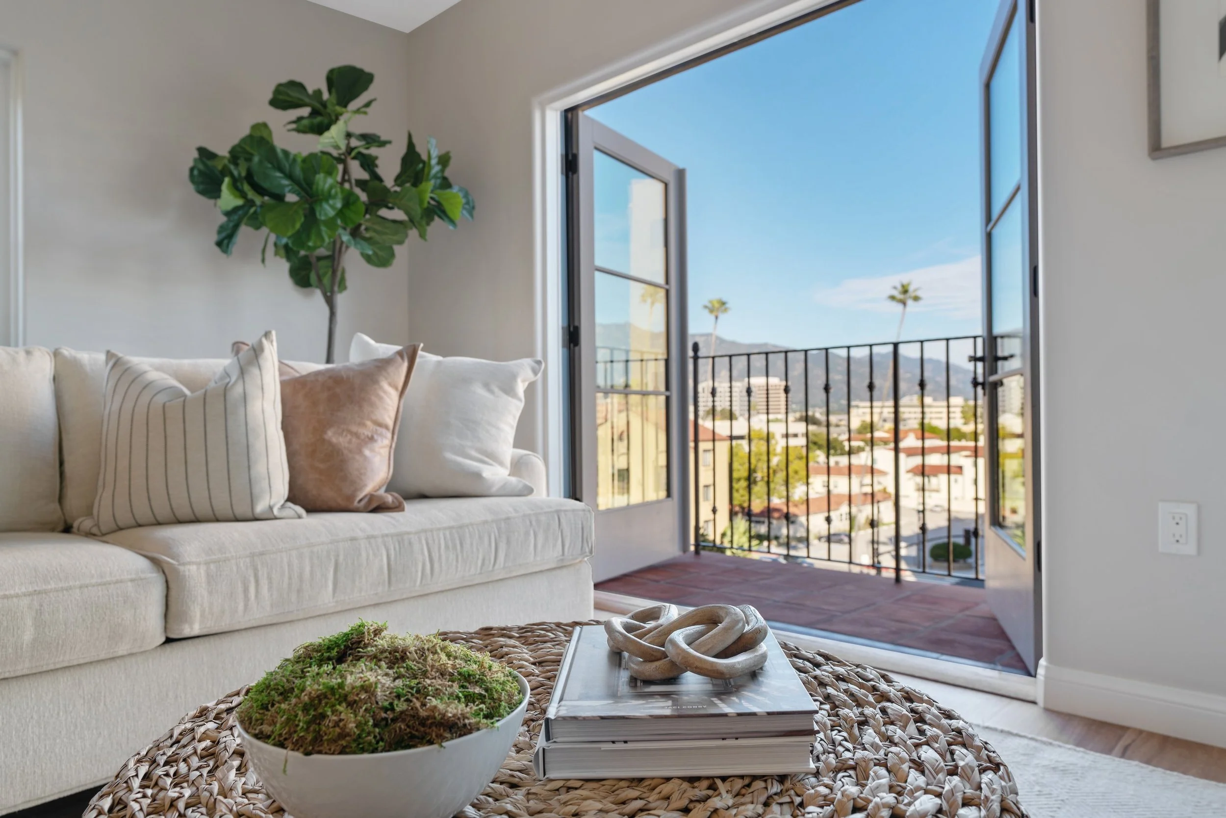 Bright living room at Brantwood senior apartments in Pasadena’s Playhouse Village, featuring French doors to a private balcony, neutral seating, wood-style flooring, and mountain views.
