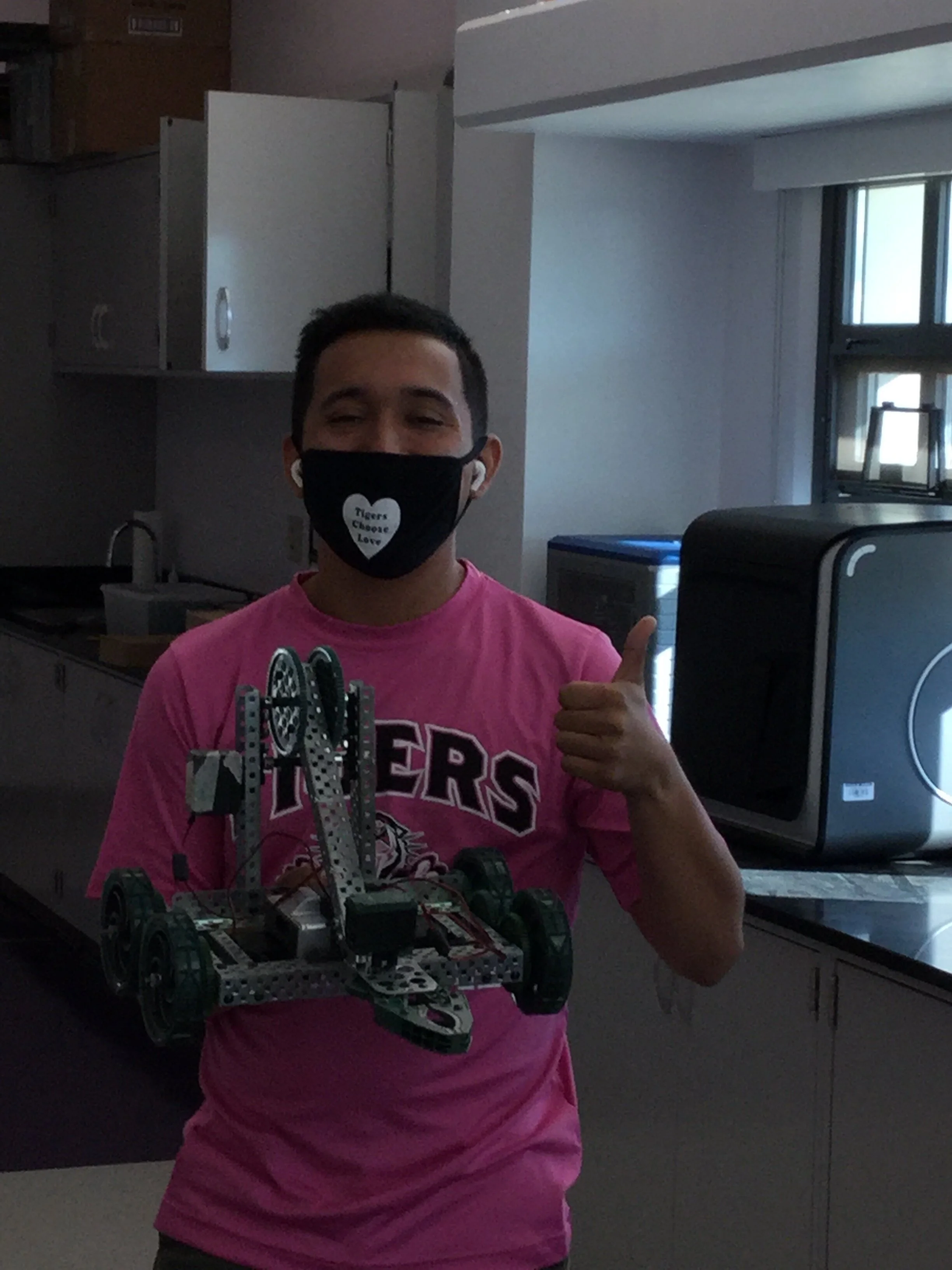 Robotics teacher Mr. Saad holding up a VEX robot made by the students