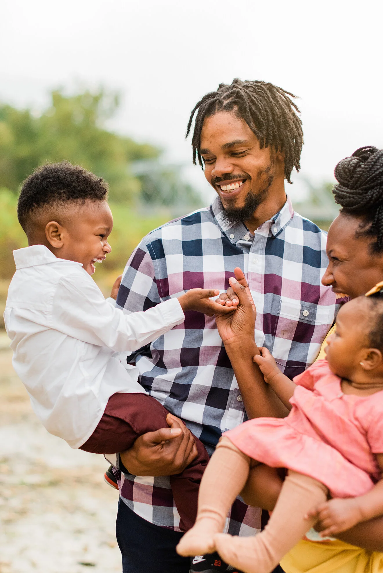 A candid moment of a father and mother being silly with their kids during their family pictures. Maryland family photo shoot Gambrill Mill photography location family photos outfit inspiration plaid shirt end of summer family photo shoot kids laughi