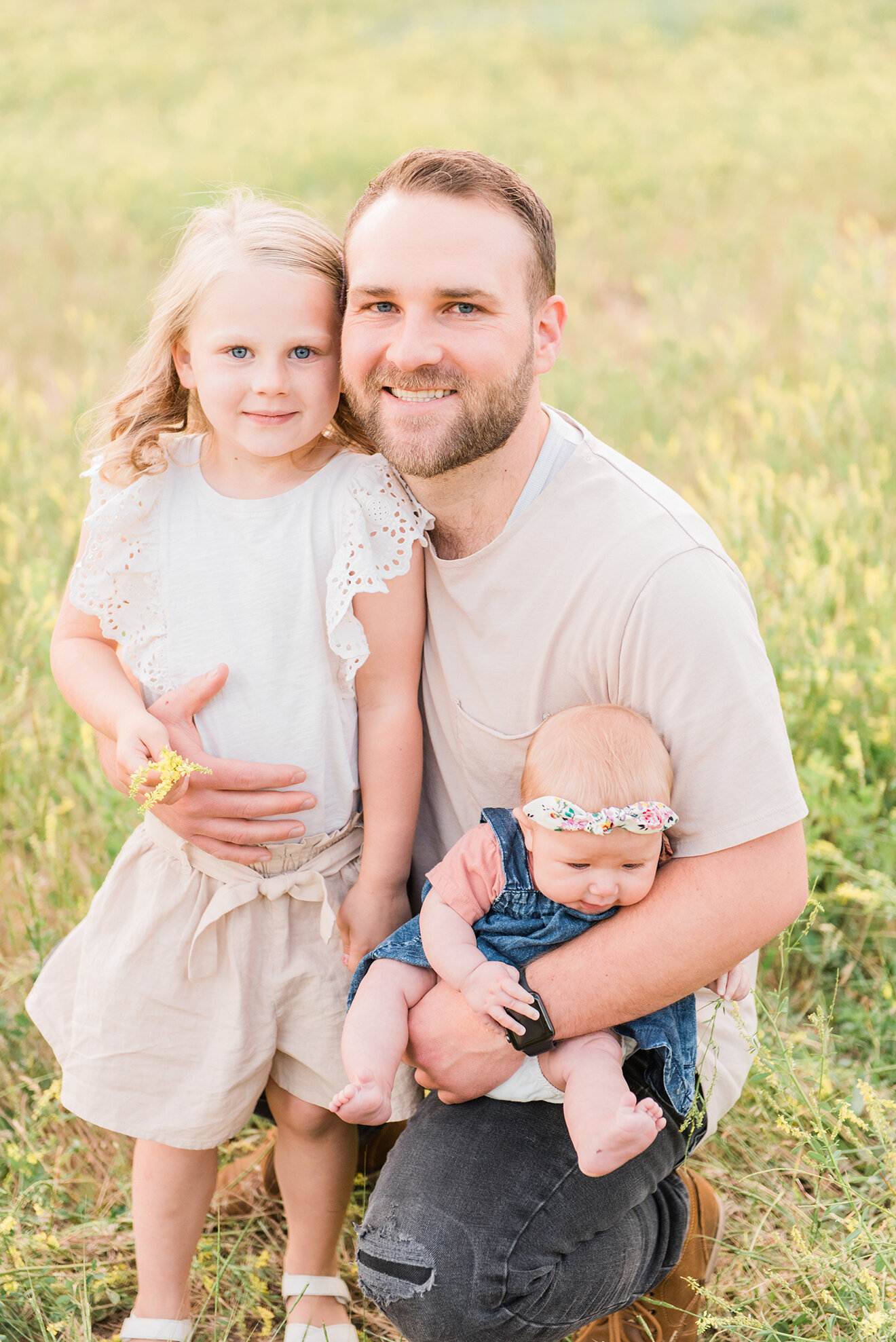  Father and his two daughters sit together in the grass in a bright and airy summer family session in Utah. Jacquie Erickson Photography professional Utah family photographer father and daughter pose inspiration newborn outfit inspiration for summer 