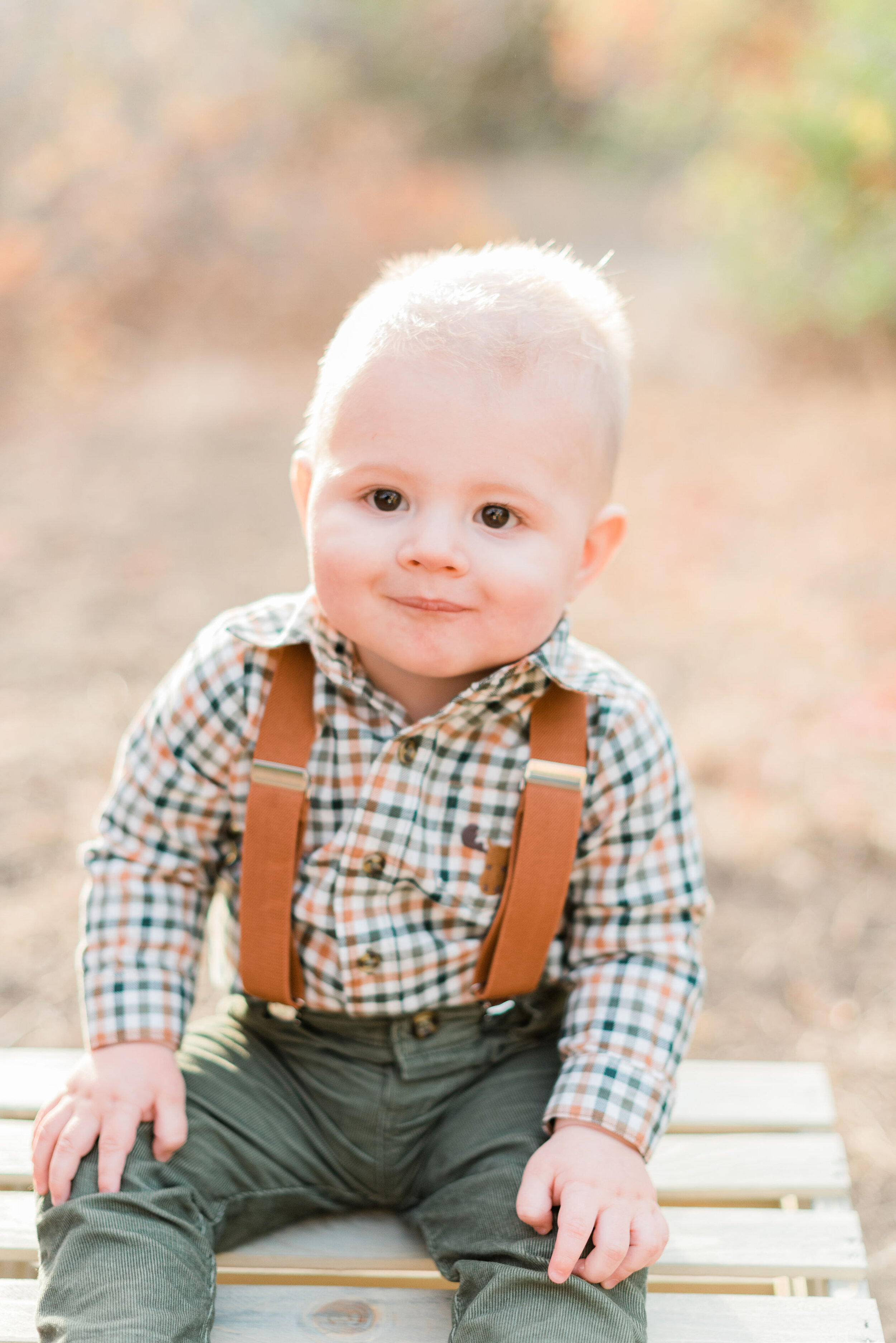  Adorable toddler boy sits on a crate in his leather suspenders in an Autumn family session in Lambert Park. Alpine, Utah Jacquie Erickson Photography toddler pose inspiration resting his hands on his knee outfit inspiration for fall family photo sho