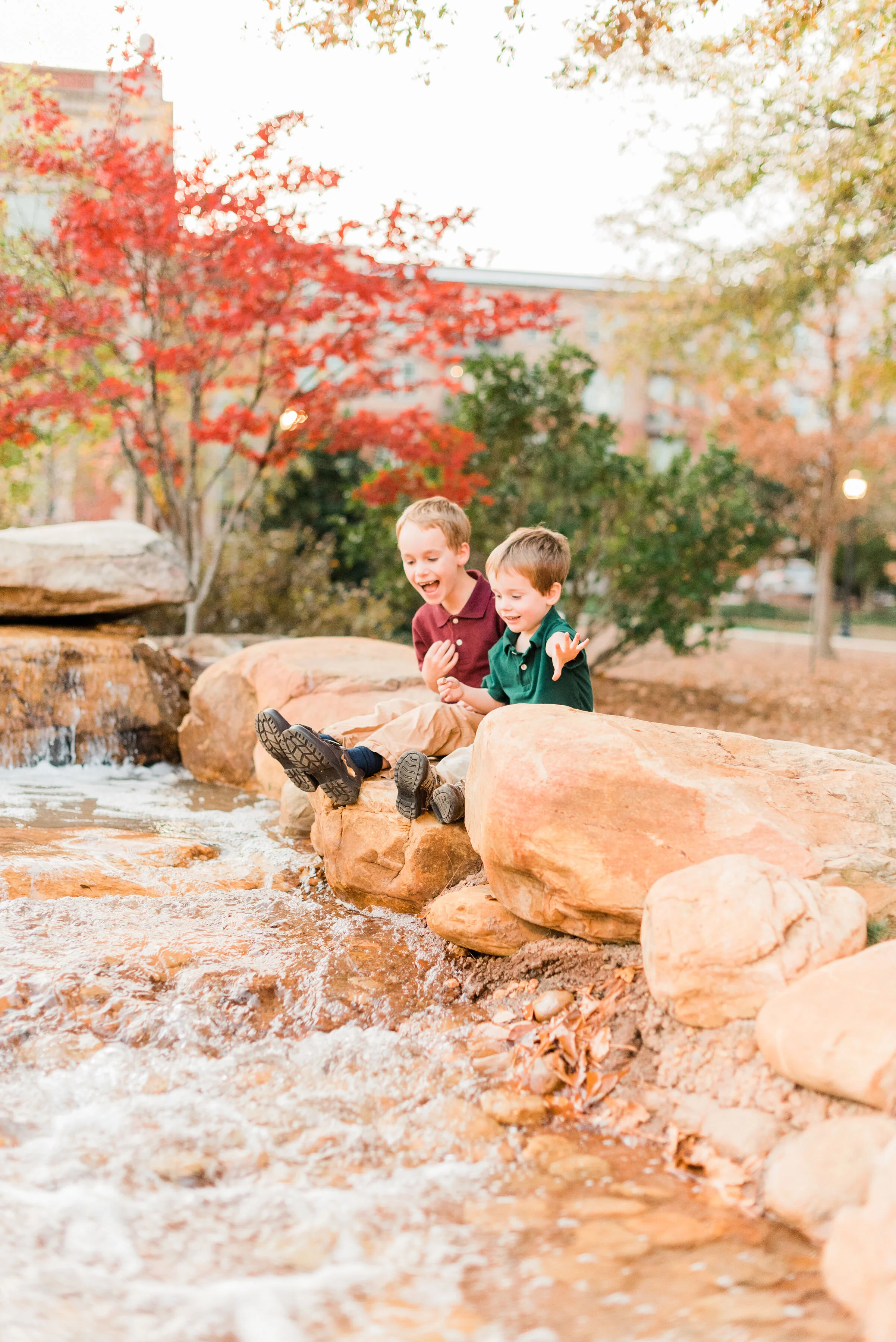  These cute two brothers play together in the rocks and water during their autumn time family pictures in Maryland with Jacquie Erickson Photography. Two brothers playing win the water splash water candid moments red leaves autumn time photography #j