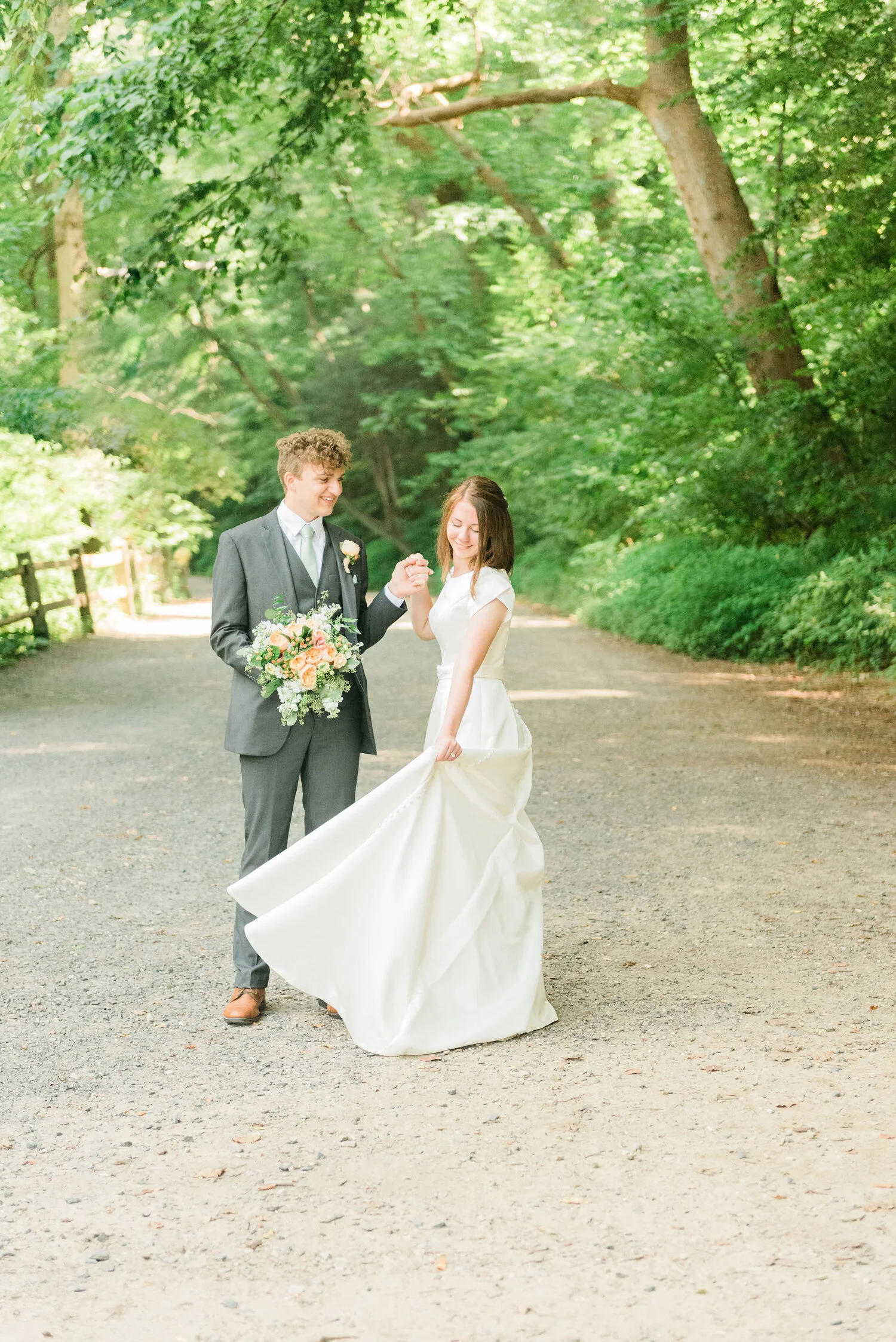  A groom holds his bride’s bouquet while she twirls in Logan Square Park in Philadelphia. wedding pictures in a park wedding dress inspiration Bride and groom pose ideas wedding bouquet ideas outdoor wedding photos cute wedding poses wedding dress wi