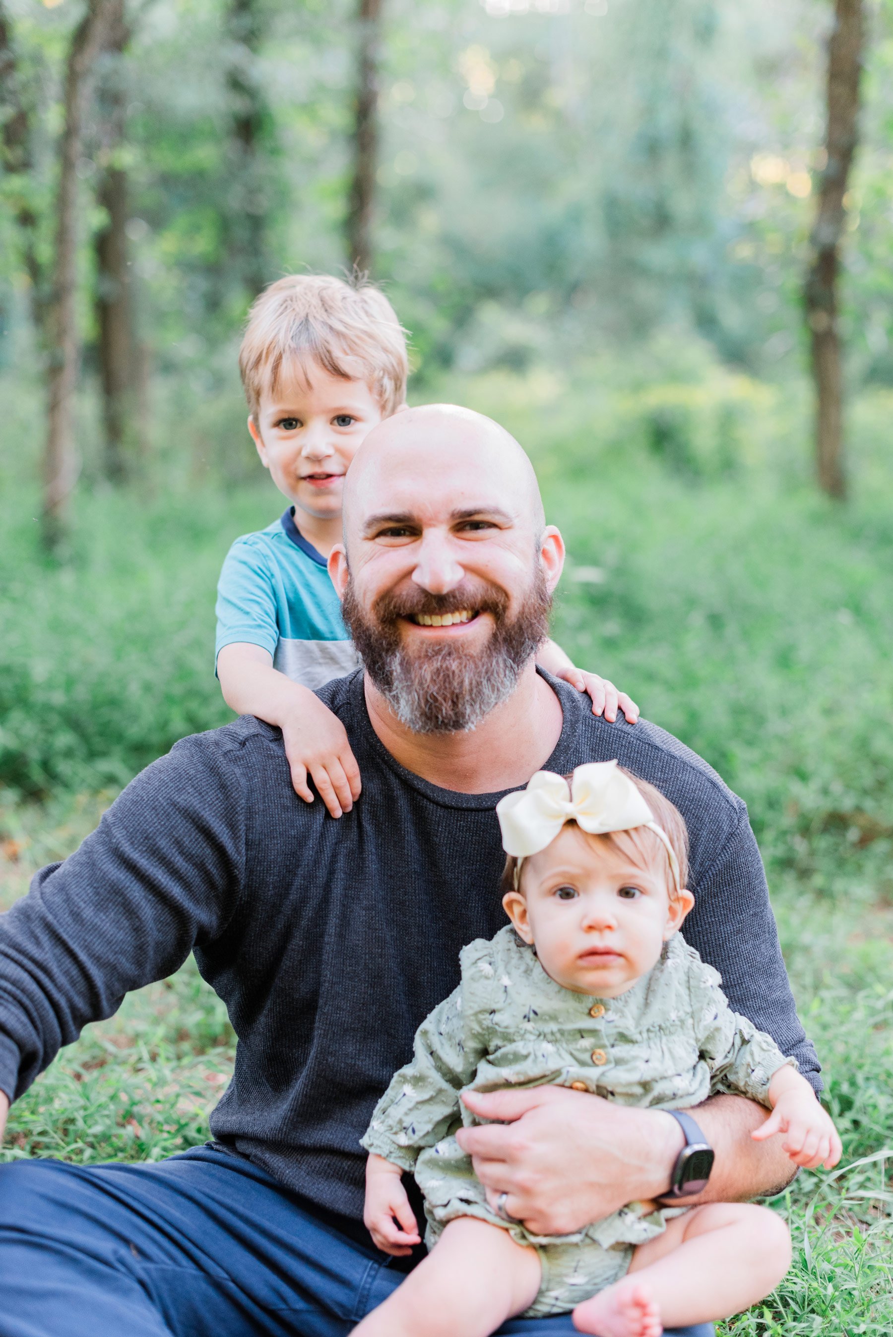    A daddy and his young son and daughter smile for the camera during an outdoor Georgia family photo session.#peachtreecityphotographer #familyphotographersenoia #outdoorfamilyphotos #familyphotoswithkids #fayettevillefamilyphotographer #fallfamilyp