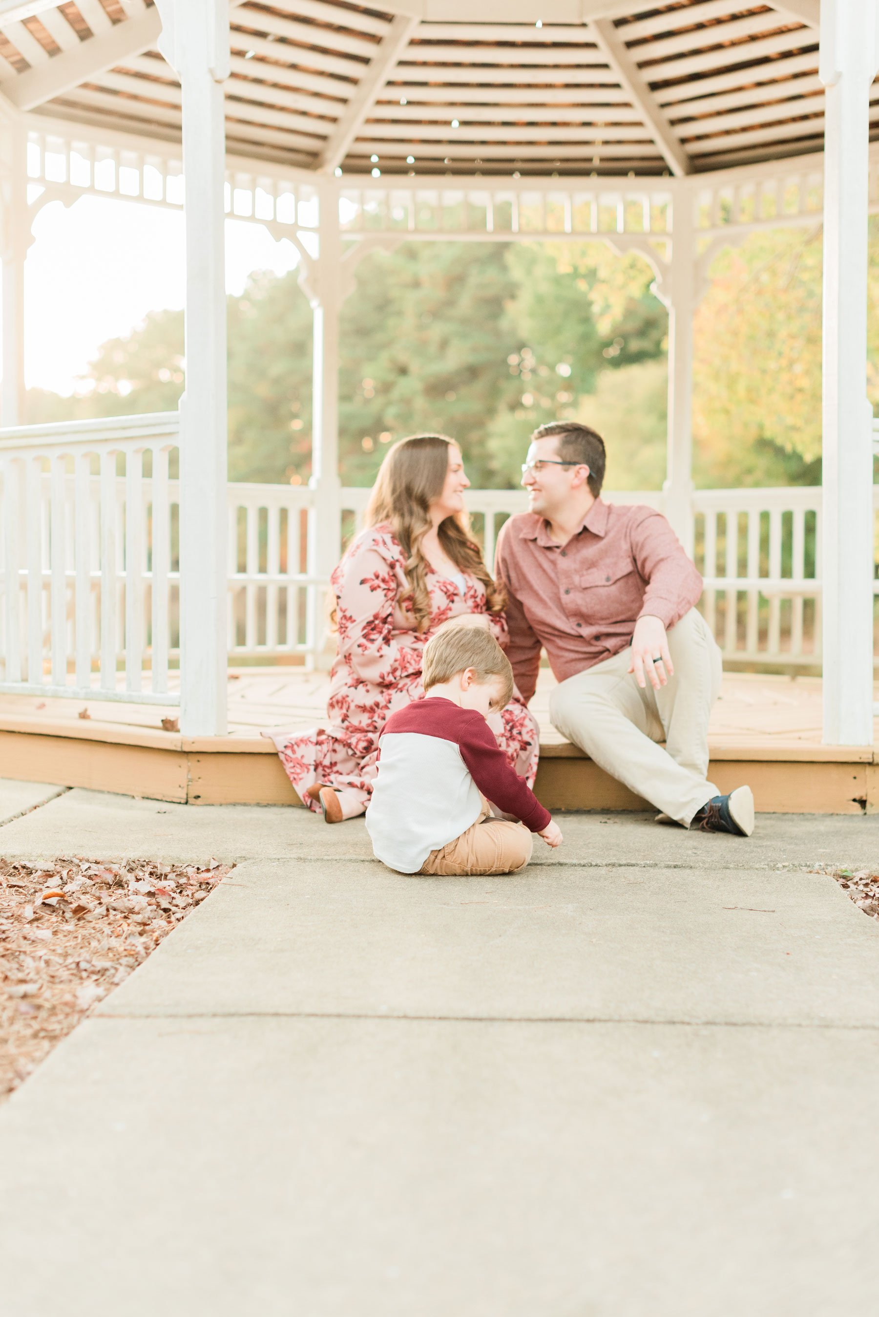  A pregnant woman looks into the eyes of her husband while their two-year-old son plays on the sidewalk in front of them. Atlanta Georgia Sandy Springs Sharpsburg Roswell&nbsp; #familymaterintyphotos #pregnacyphotoshoot #fathersonphoto #peachtreecity