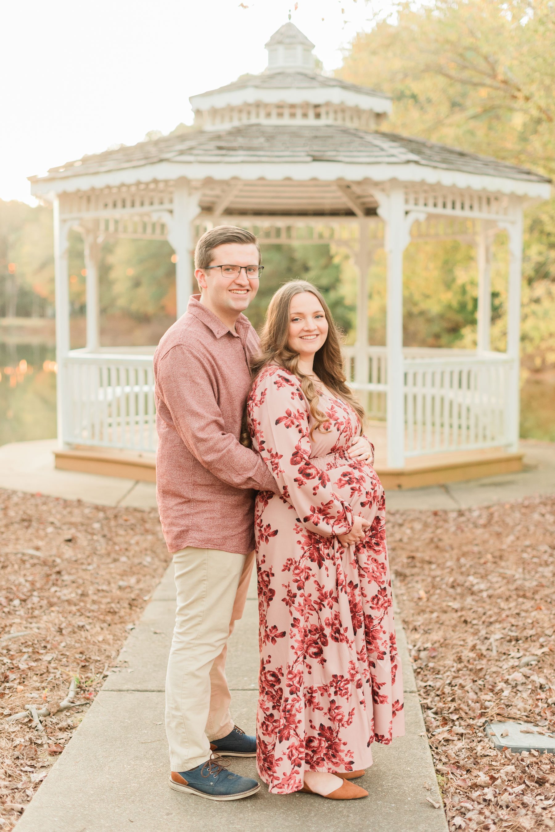  A husband stands behind his pregnant wife in front of a gazebo during their maternity photo session. Atlanta family photographer Sandy Springs Sharpsburg Roswell&nbsp; #familymaterintyphotos #pregnacyphotoshoot #littleboyphoto&nbsp; #peachtreecity #