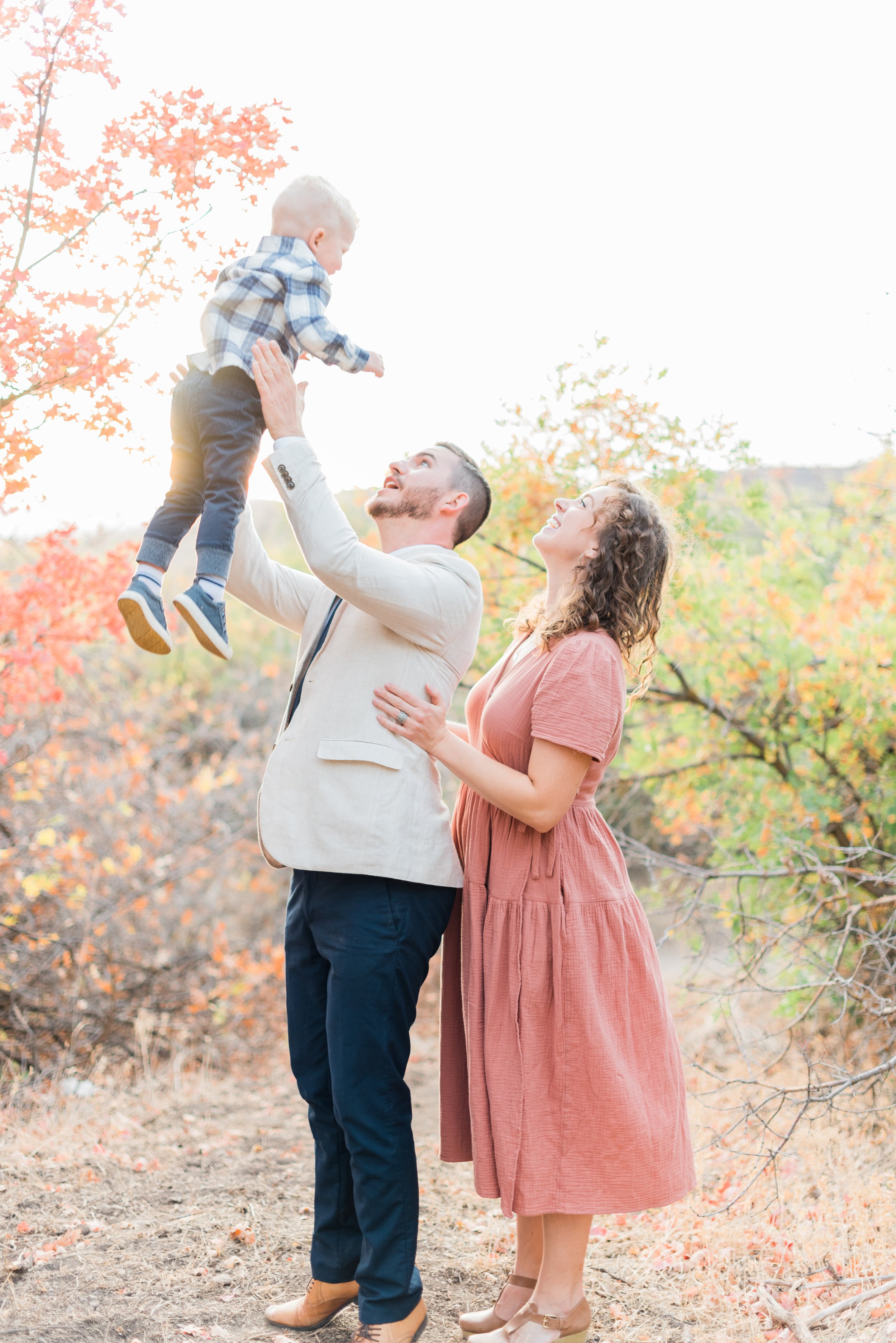  A dad throws his son up in the air with his wife behind him during a family photoshoot in the fall. Natural laughter poses personalized photoshoot #atlantafamilyphotographer #familiesofinstagram #familypics #GeorgiaFamilyPhotographer #PeachtreeFamil