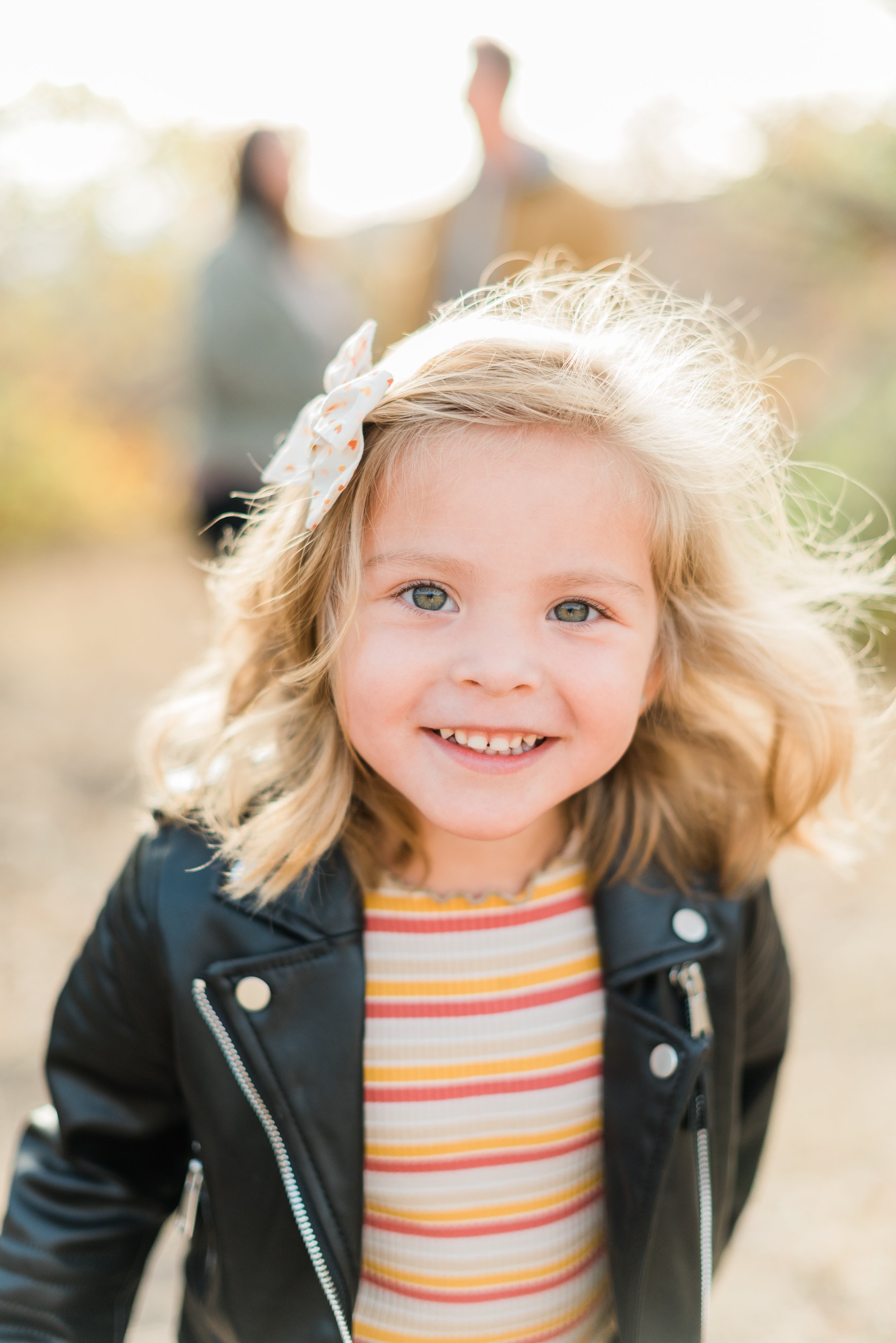  A little girl smiles for the camera with her parents blurred in the background. Jacquie Erickson Photography email templates know your clients photo timeline updates&nbsp; #postphotoshoottips #GeorgiaFamilyPhotographer #photographertips #peachtreeGA
