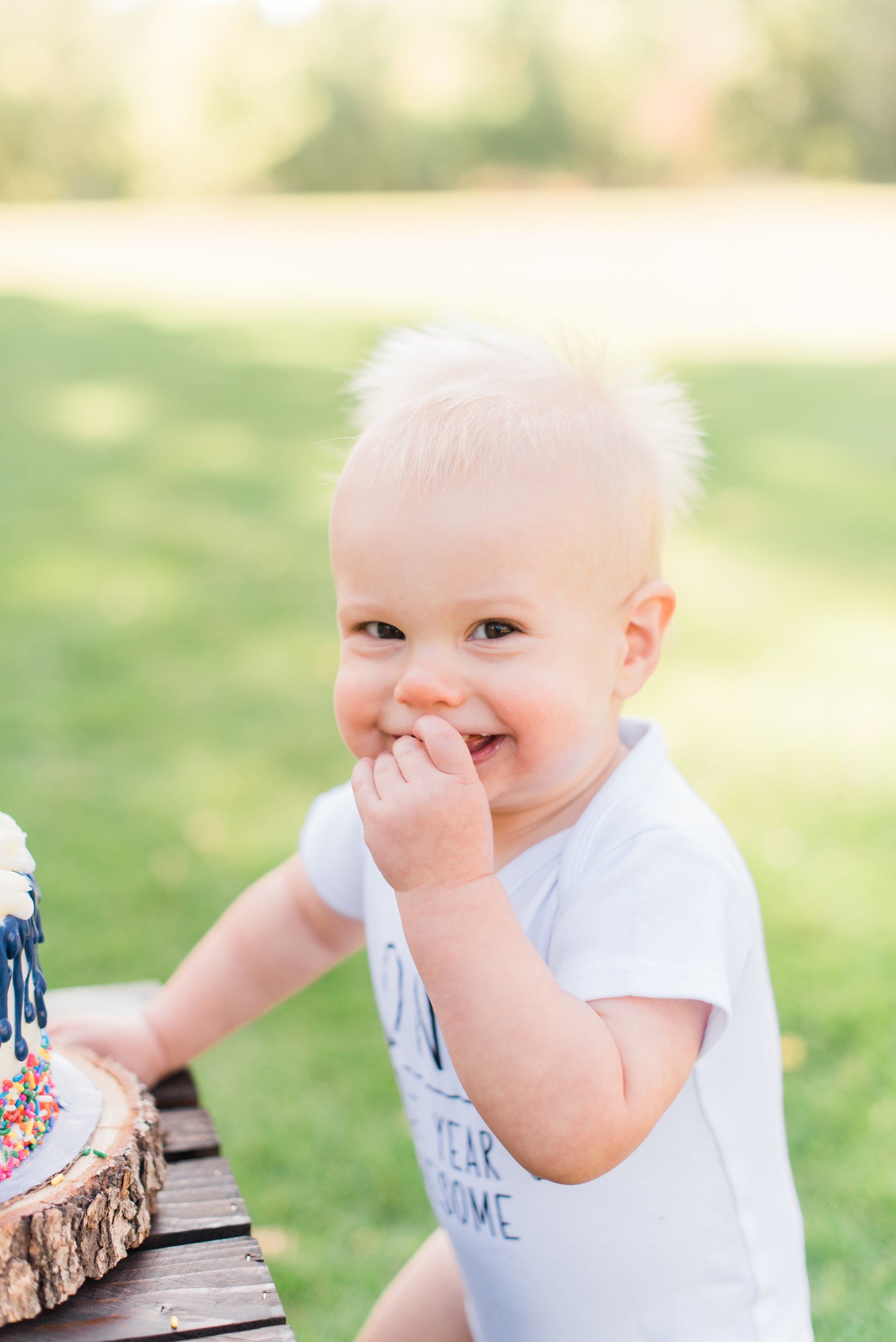  A sweet birthday boy in Peachtree City smiles during his cake smash at his first birthday party. #marylandfamilyphotographer #onlinephotographycourse #photographytips #familyphotosession #diyfamilyphotos #kidportraits #cakesmashphotos #firstbirthday