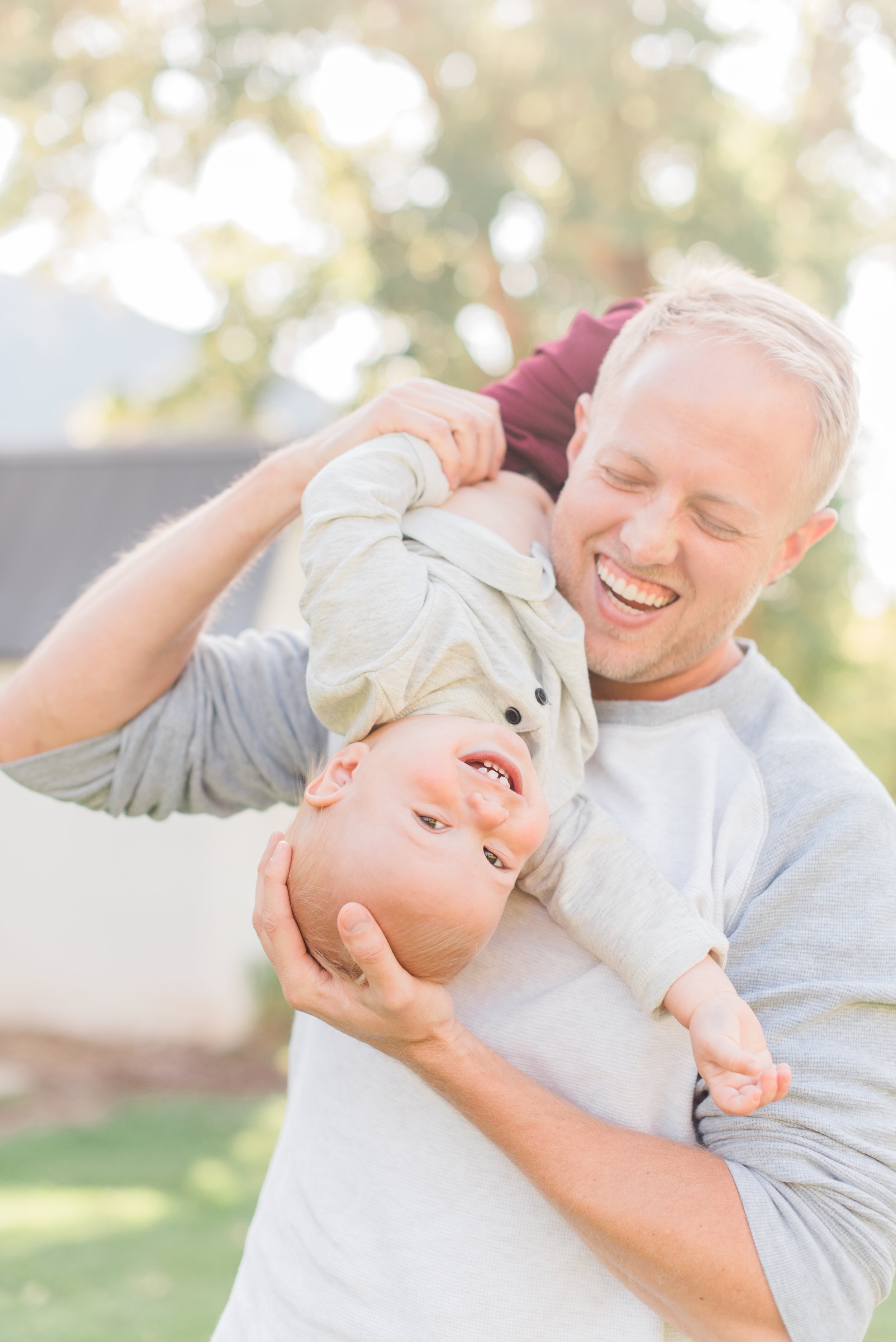  A dad and his son are captured mid-laugh by photographer Jacquie Erickson on a beautiful summer day. Happy family father-son summertime candid shot pure joy #candidkidsphoto #daddysboy #midlaugh #summertime #georgiaphotographer 