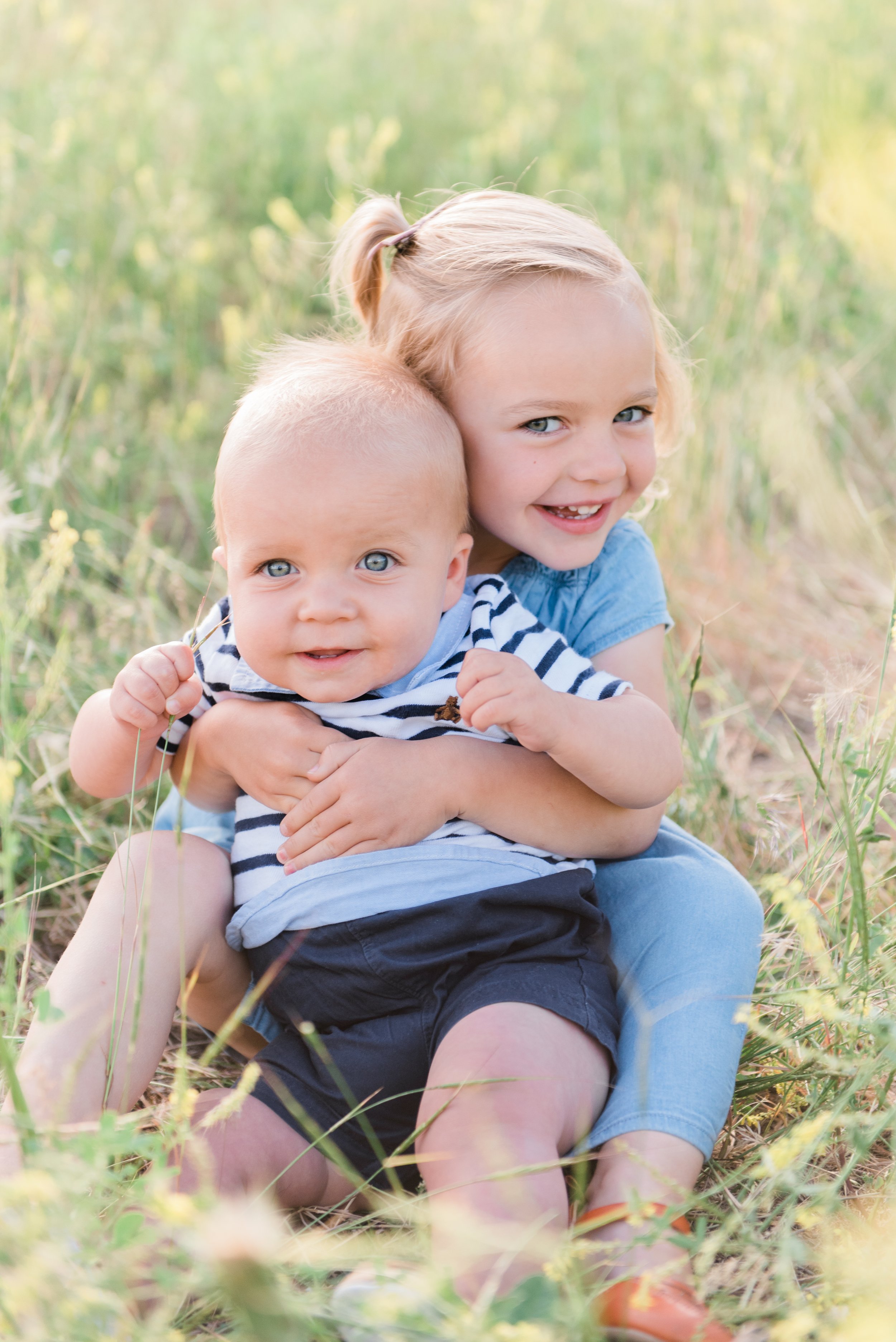  A baby brother is held on the lap of his big sister in a summer field. Young children photoshoot brother and sister summer photos Jacquie Erickson photography #brothersisterphoto #babybrother #jacquieerickson #youngkids #georgiaphotographer 