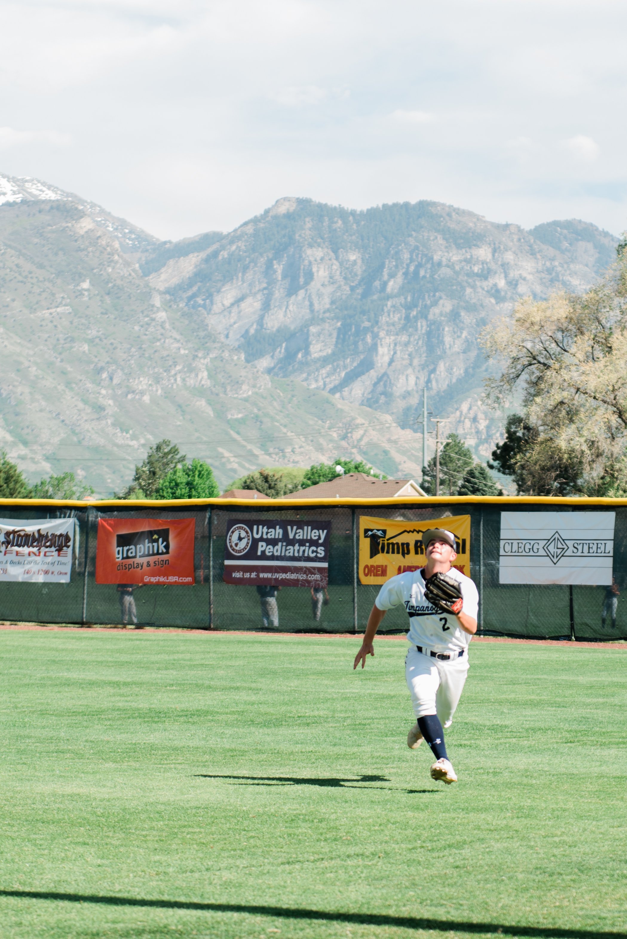  The majestic mountains are the background of this action photo of a young boy midstride in a summer baseball game. Baseball mountains green baseball field sports action shot #baseball #youthsportphoto #baseballactionshot #mountainbackground #georgia