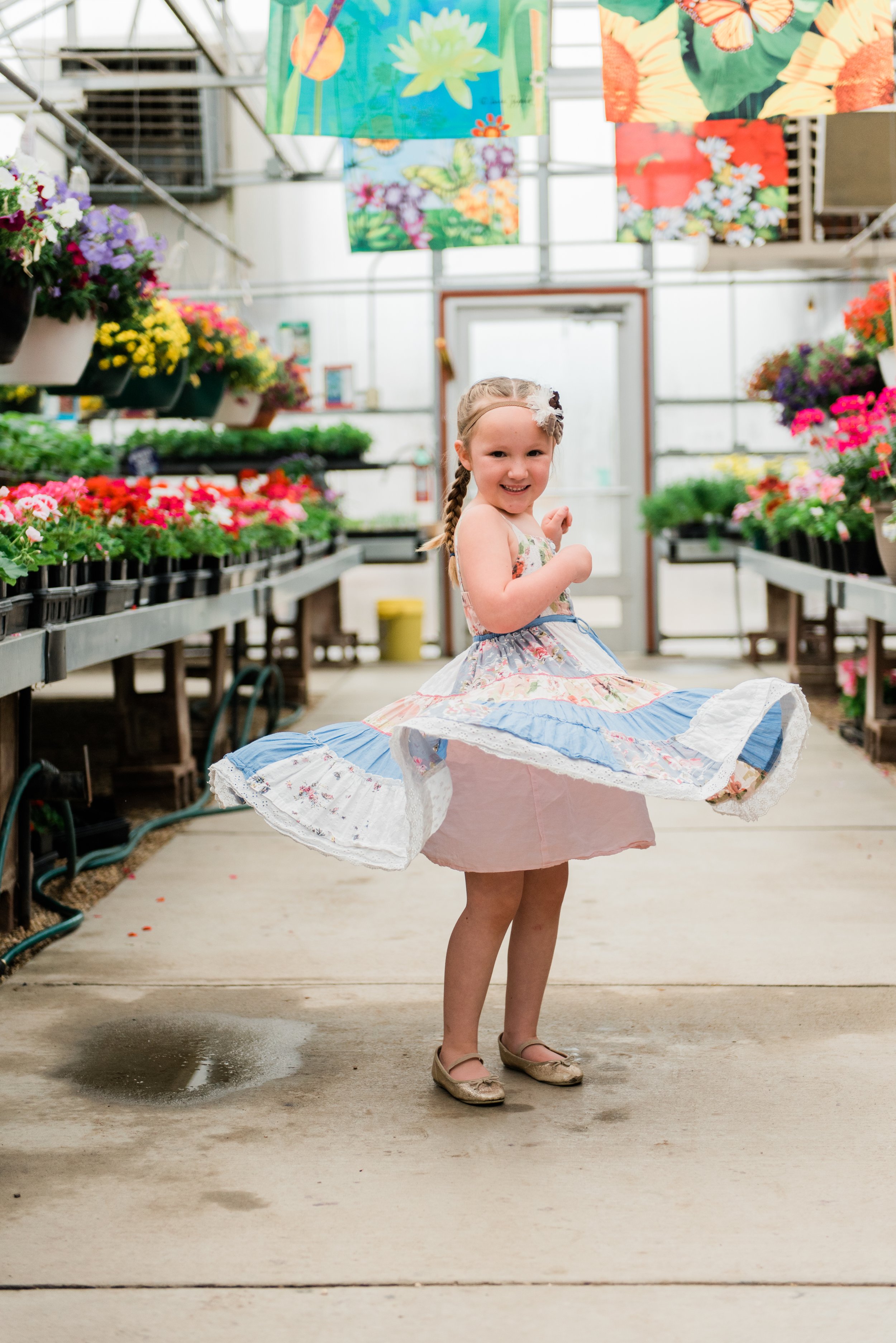  A little girl smiles mid-twirl in a greenhouse full of flowers. Natural posed photo captured personality posing guide Marietta GA momtog course #diyphotography #firstdayofschoolphotos #capturethemoment #littlegirlphoto 