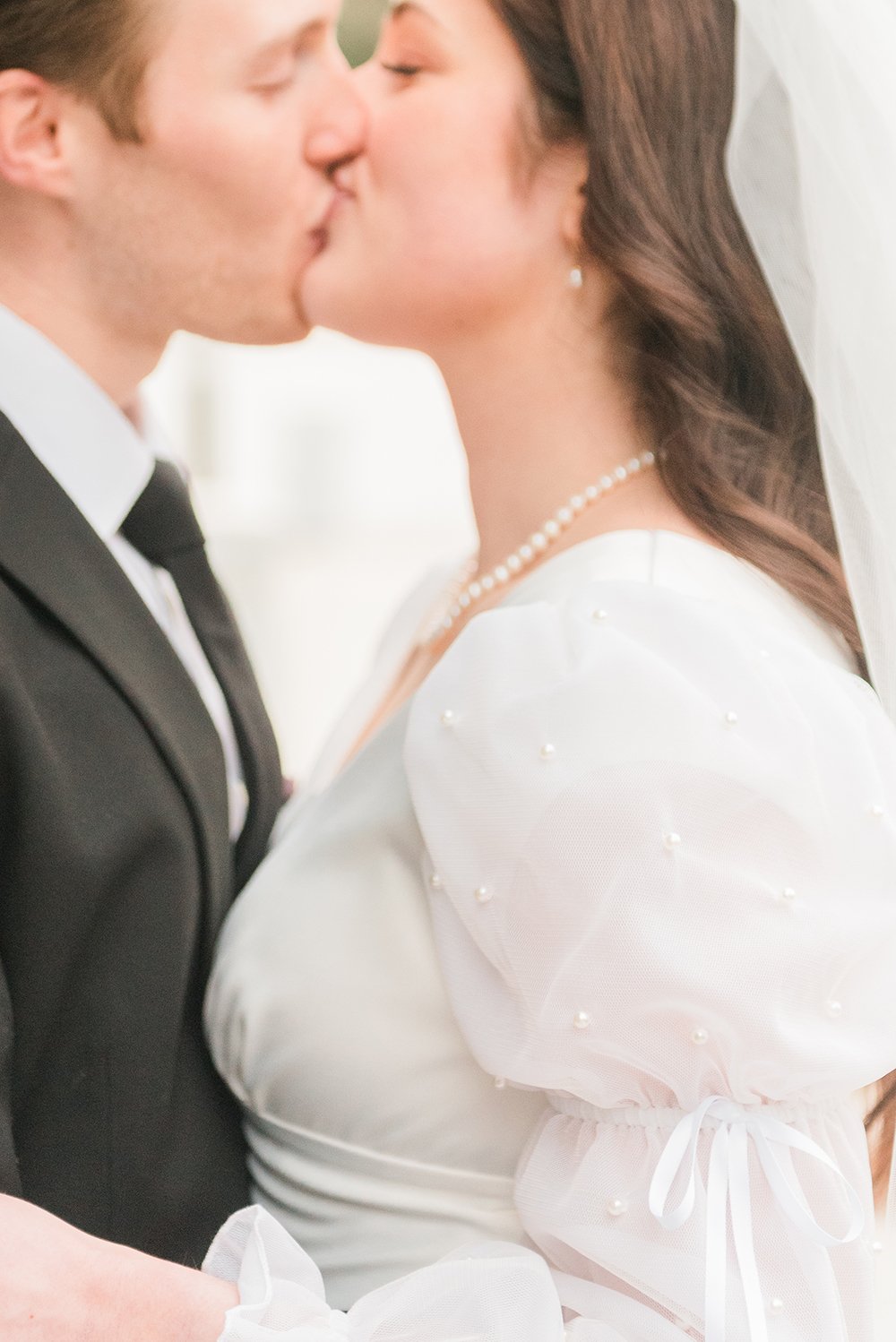  The focus of this wedding photo by Jacquie Erickson is the detail of the bride's dress, while the couple is out of focus kissing. Detail focus wedding picture modest wedding dress&nbsp; wedding photographer Senoia Newnan #weddingphotographer #ldswed