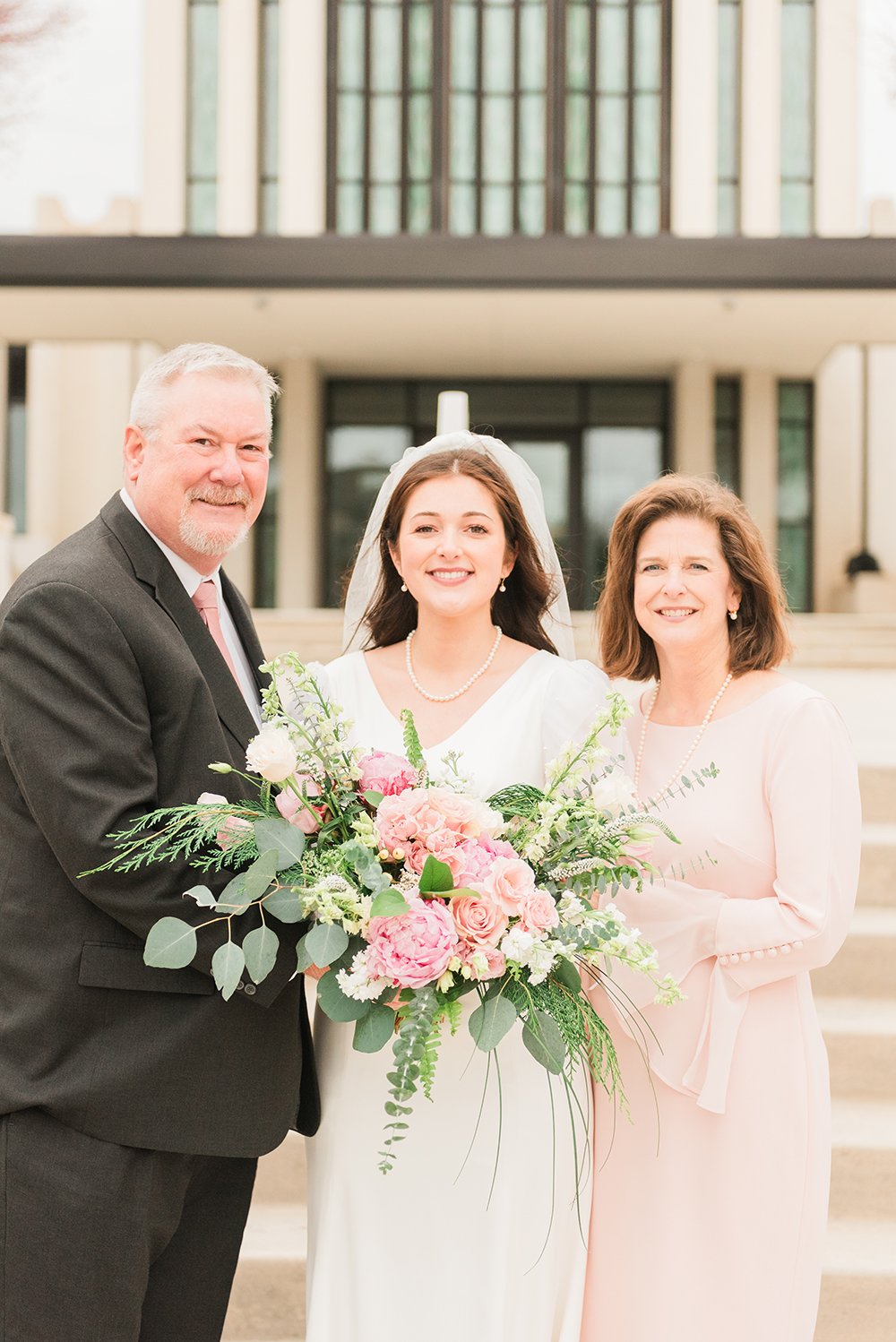  A bride stands with her mom and dad holding her wedding bouquet in front of the Atlanta, Georgia LDS temple. wedding photographer Atlanta photographer Sharpsburg Roswell #weddingphotographer #ldsweddings #atlantatemple #jacquieerickson #parentsofthe