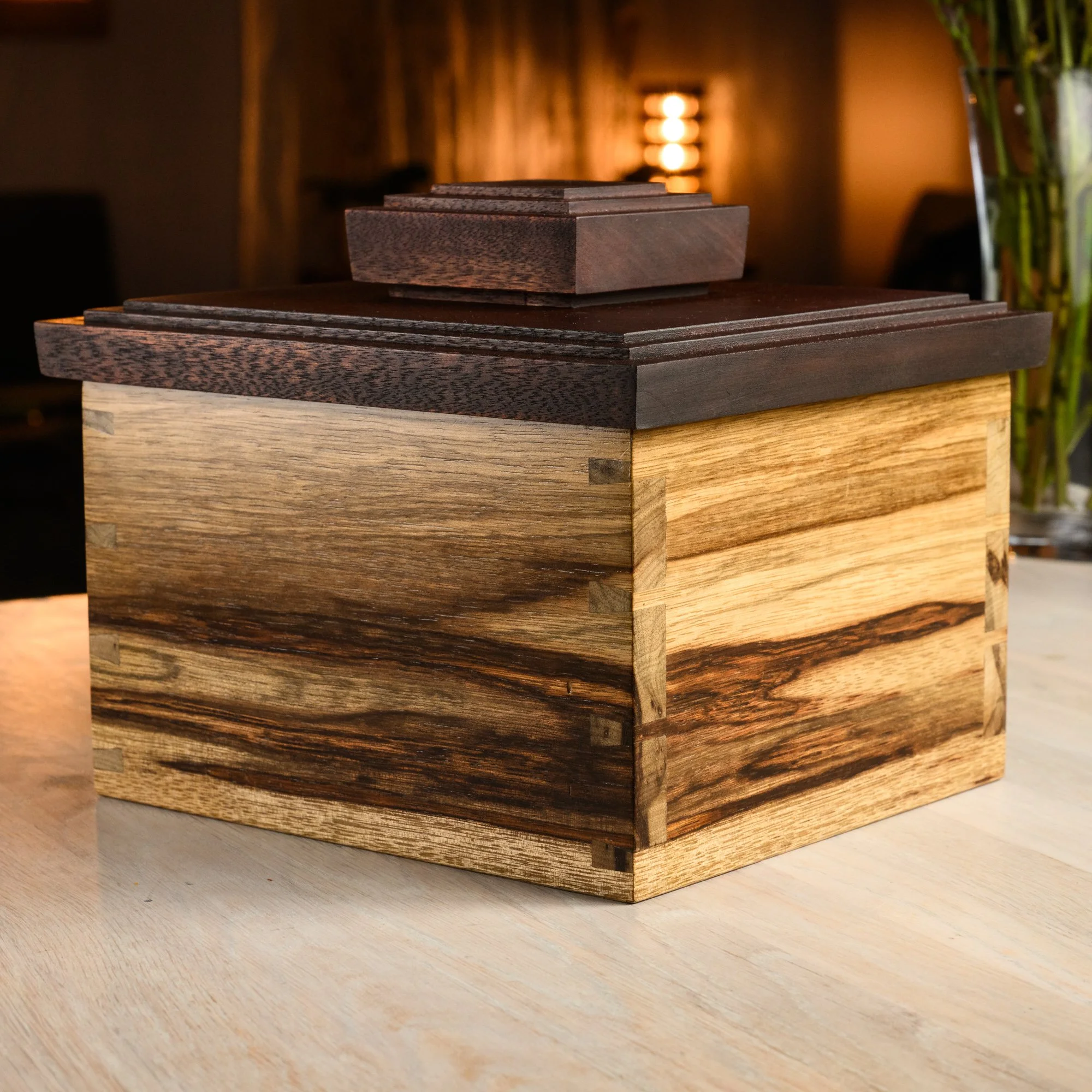 A handcrafted wooden box with a darker lid and a lighter base, featuring intricate dovetail joints.
