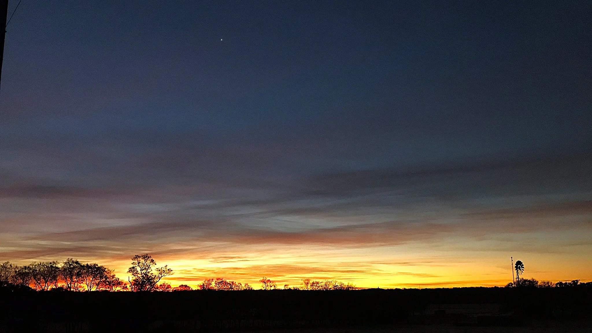 A sky at sunrise dark above, light on the horizon, with a windmill visible on the lower right and a single star high in the sky.