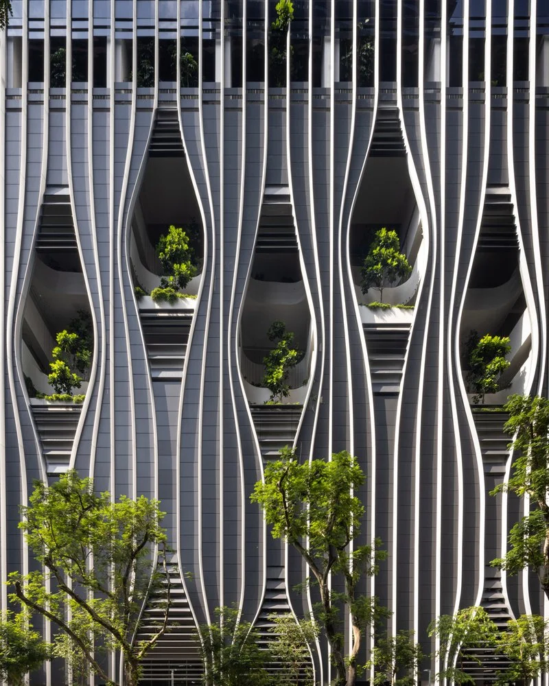新加坡的CapitaSpring,一座現代高層建築的外牆,由垂直的波浪狀白色和灰色線條構成,其間點綴著多個橢圓形的開口,每個開口內都種植著綠色植物。