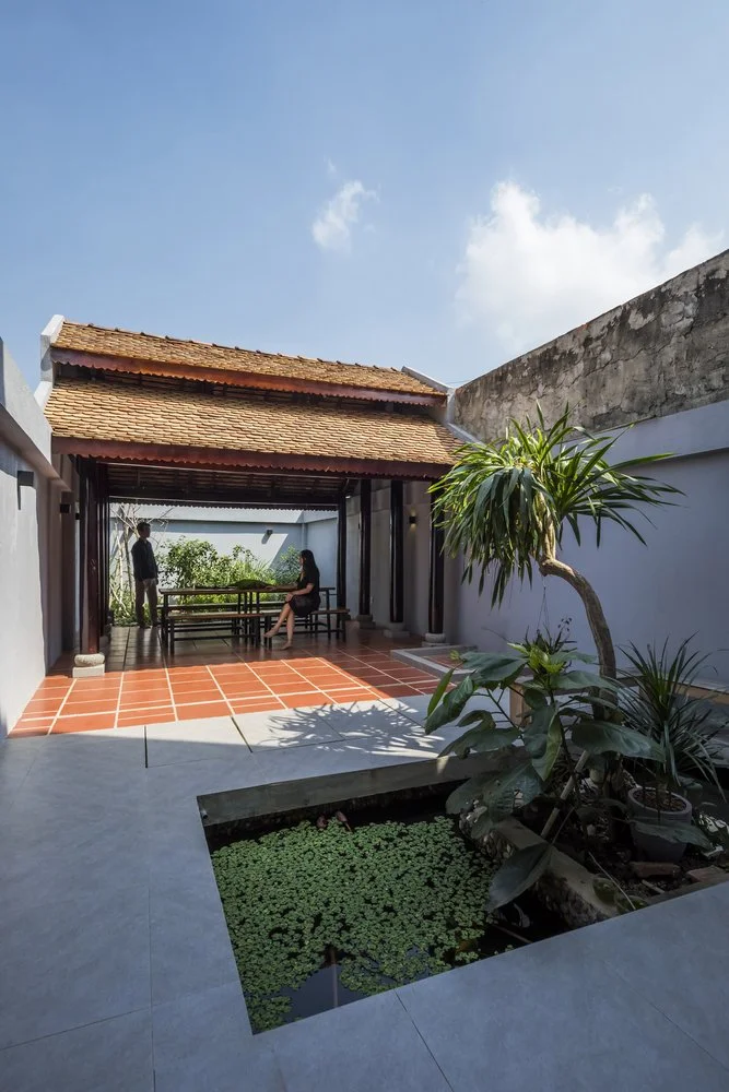 位於越南的2Hien House,由CTA | Creative Architects設計,一個傳統風格的亞洲庭院,設有紅瓦屋頂的開放式涼亭,涼亭內擺放著戶外家具。庭院中央有一個種滿水生植物的方形水池,周圍是鋪設了瓷磚的地面和簡約的牆壁。