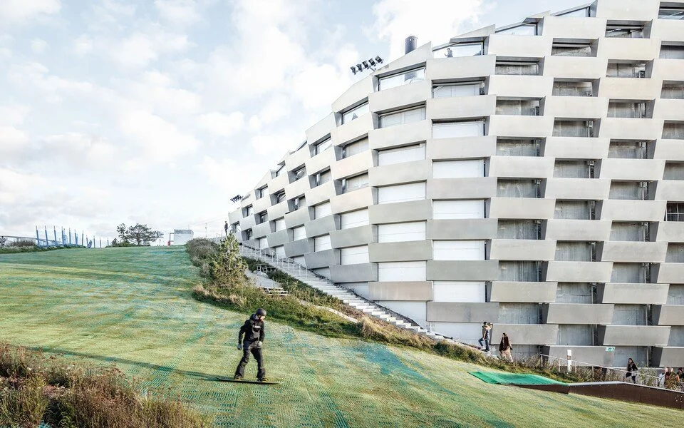 Copenhill 側面滑雪坡,市民在人工草皮上進行滑雪運動,突顯城市基礎建設的多功能性。 Side view of Copenhill’s ski slope, with people skiing on synthetic turf, highlighting the multifunctionality of urban infrastructure.