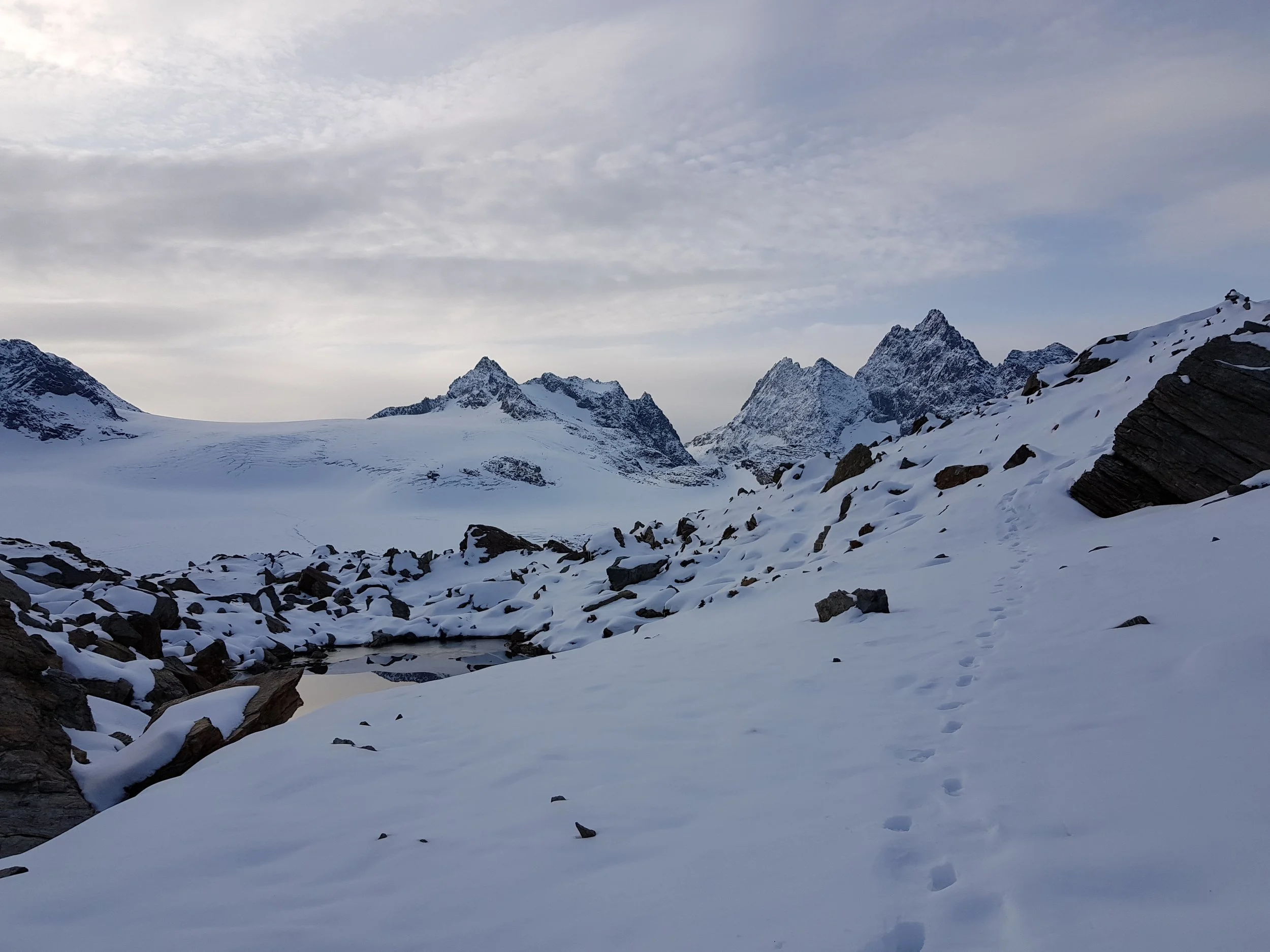 Snow-covered mountain landscape with rocky peaks and a cloudy sky.
