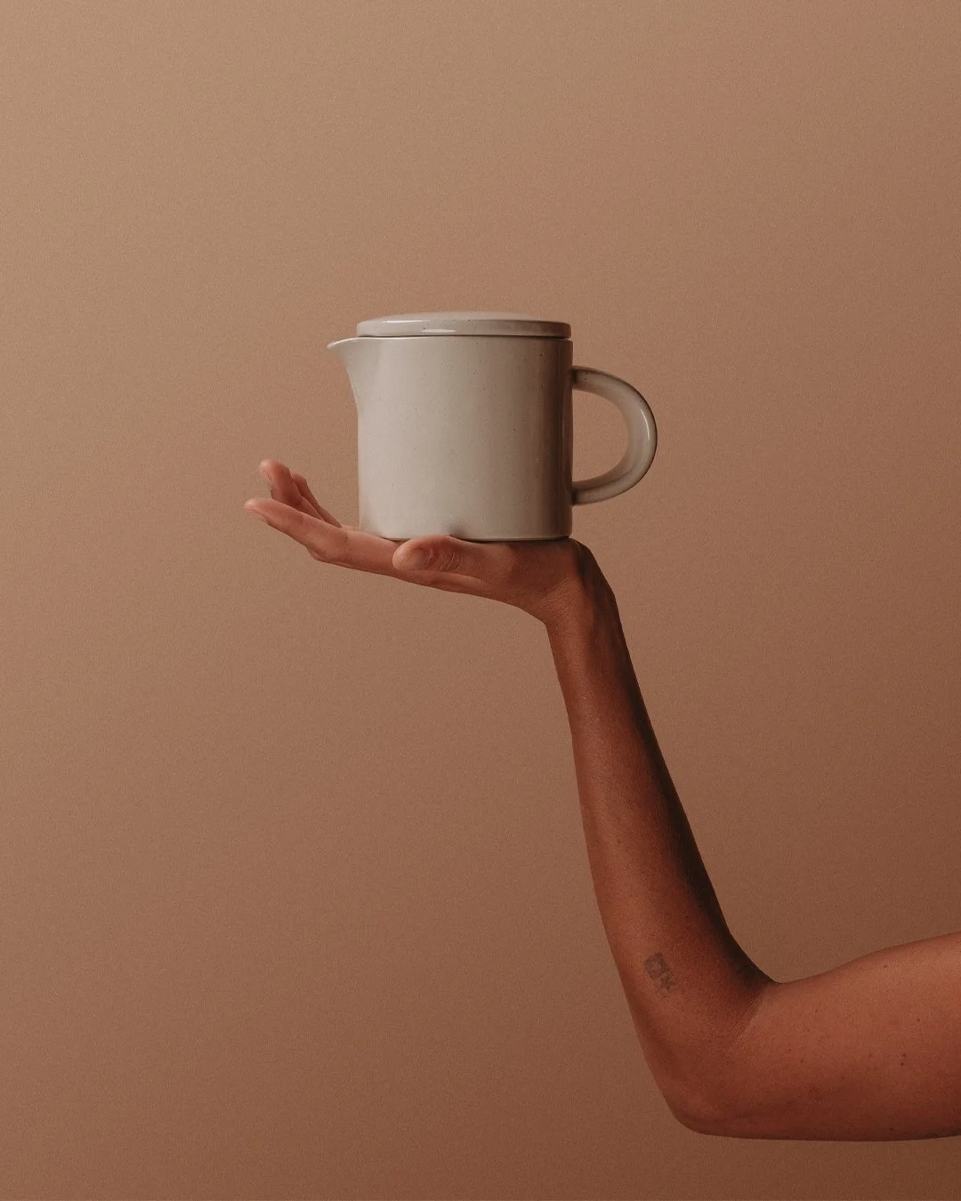 A person's hand and forearm holding a white ceramic coffee mug against a beige background.