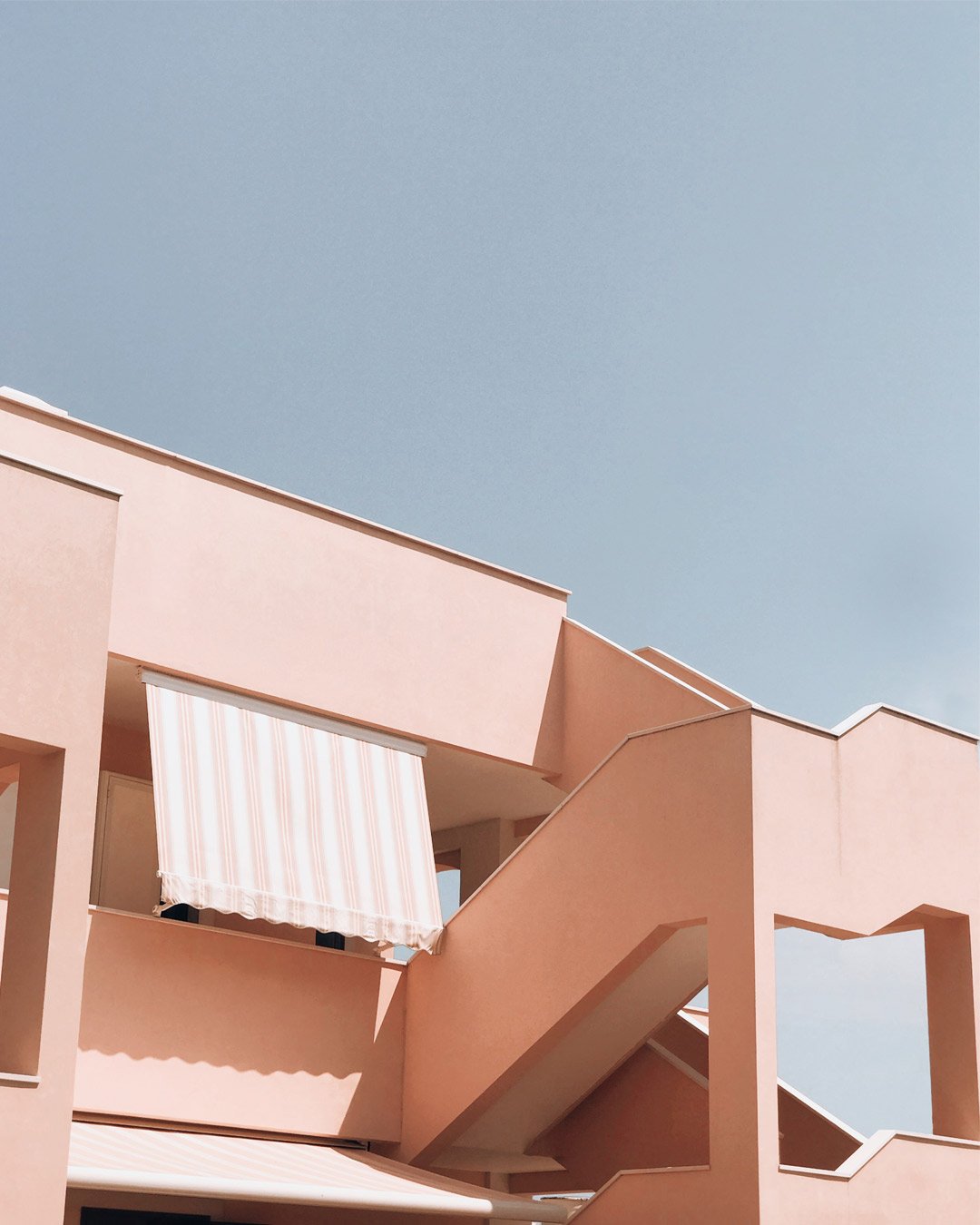 A pink building with geometric shapes and staircases against a clear blue sky.