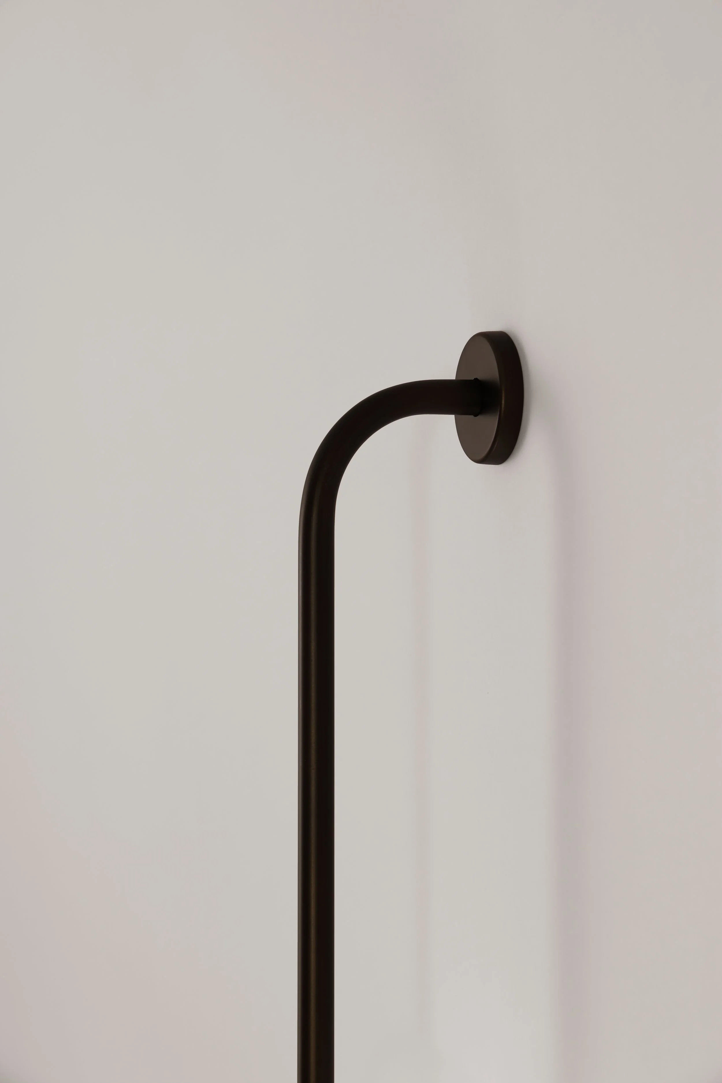 Side profile of the Drop Light II wall lamp. Detail of the minimalist curved black metal stem and the flush-to-wall mounting system for a clean architectural integration.
