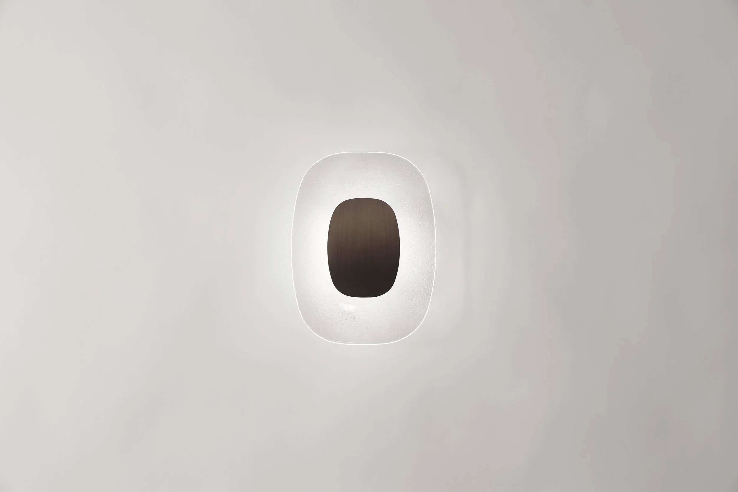 Frontal view of the Drop Light, appearing as a mineral element integrated into a minimalist architectural plane.