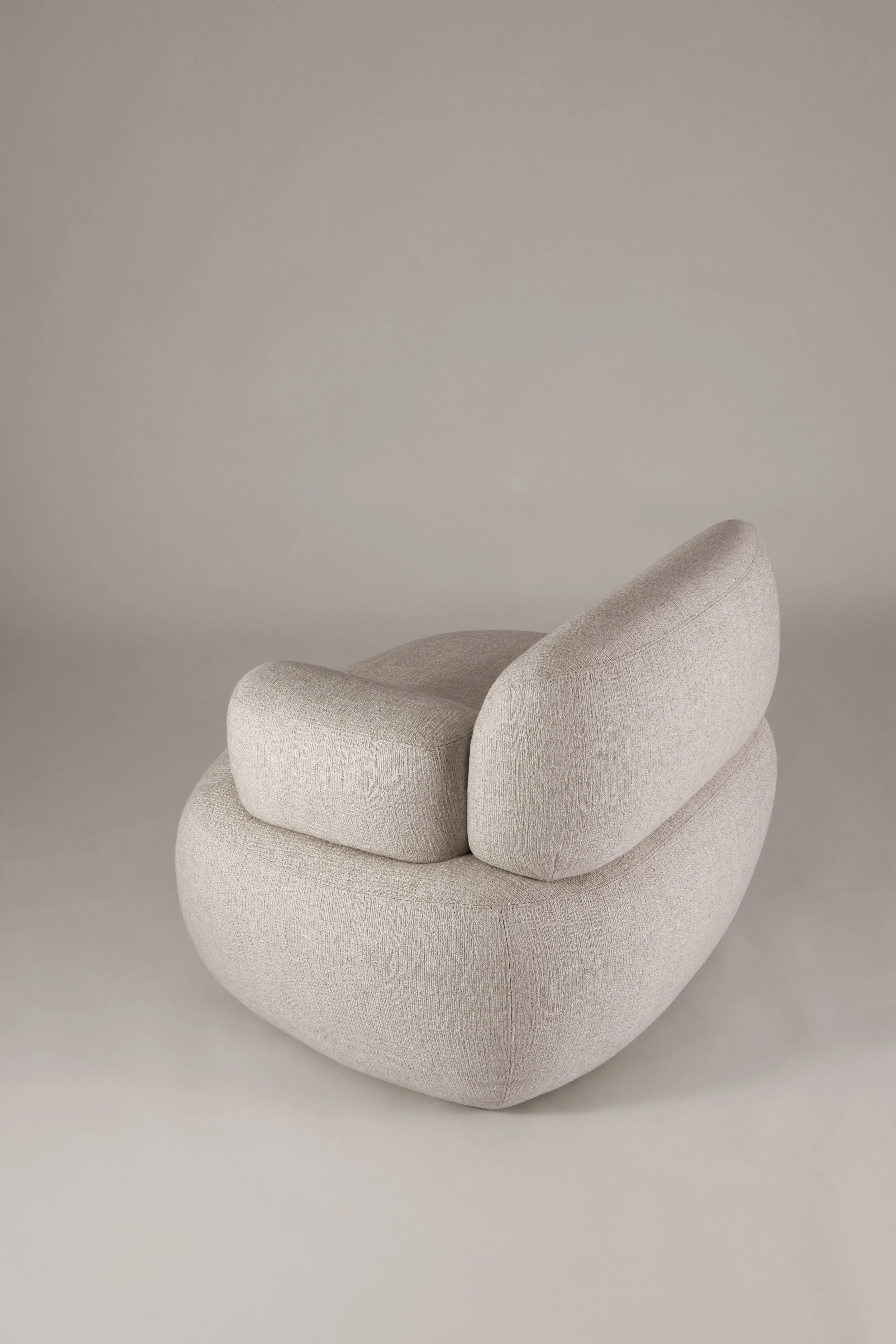 Three-quarter rear view of the Sekitei armchair, accentuating the welcoming stillness and balanced volumetric curves.